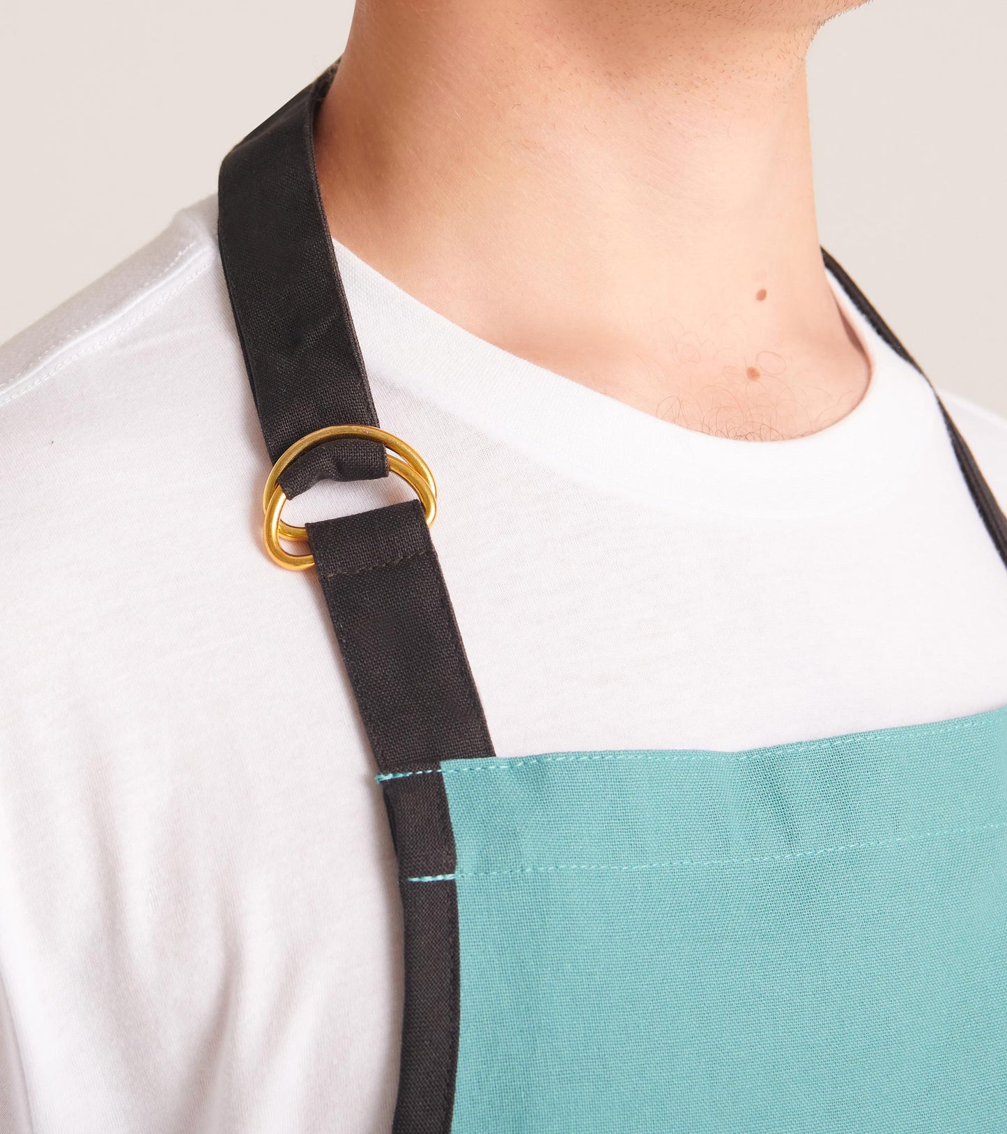 Teal apron with black straps and gold ring detail, designed for kitchen use.