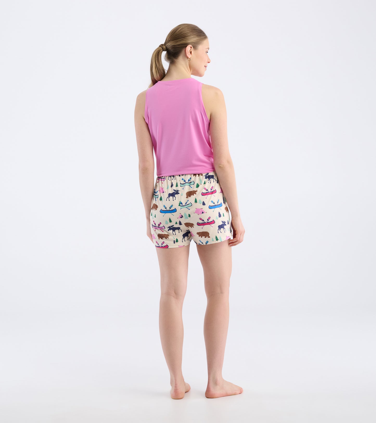 Back view of a woman wearing pink tank top and cream pajama shorts with colorful animal and nature patterns.