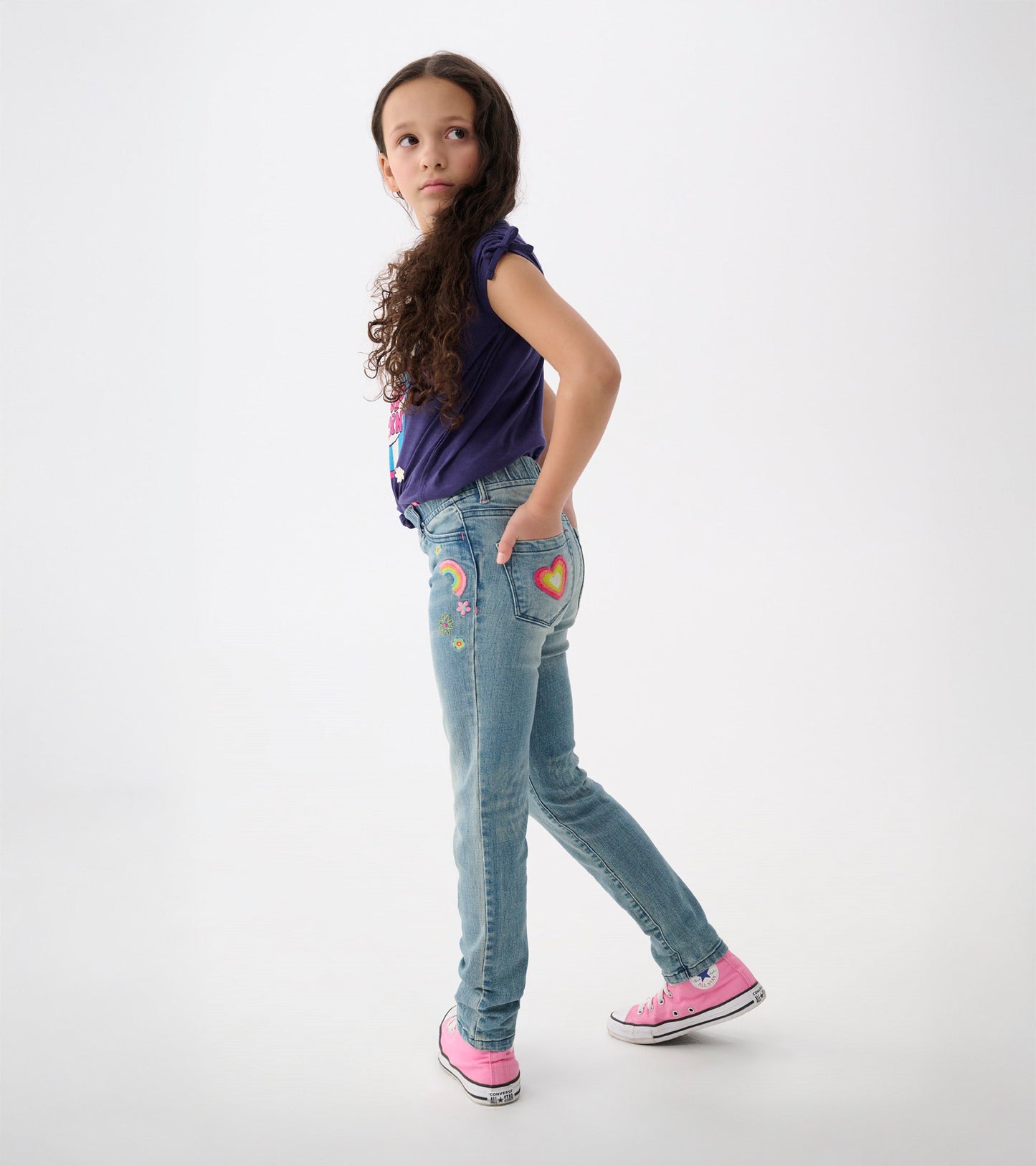 Light blue stretch jeans with colorful patches, featuring a rainbow and heart design, styled with a purple top and pink shoe…