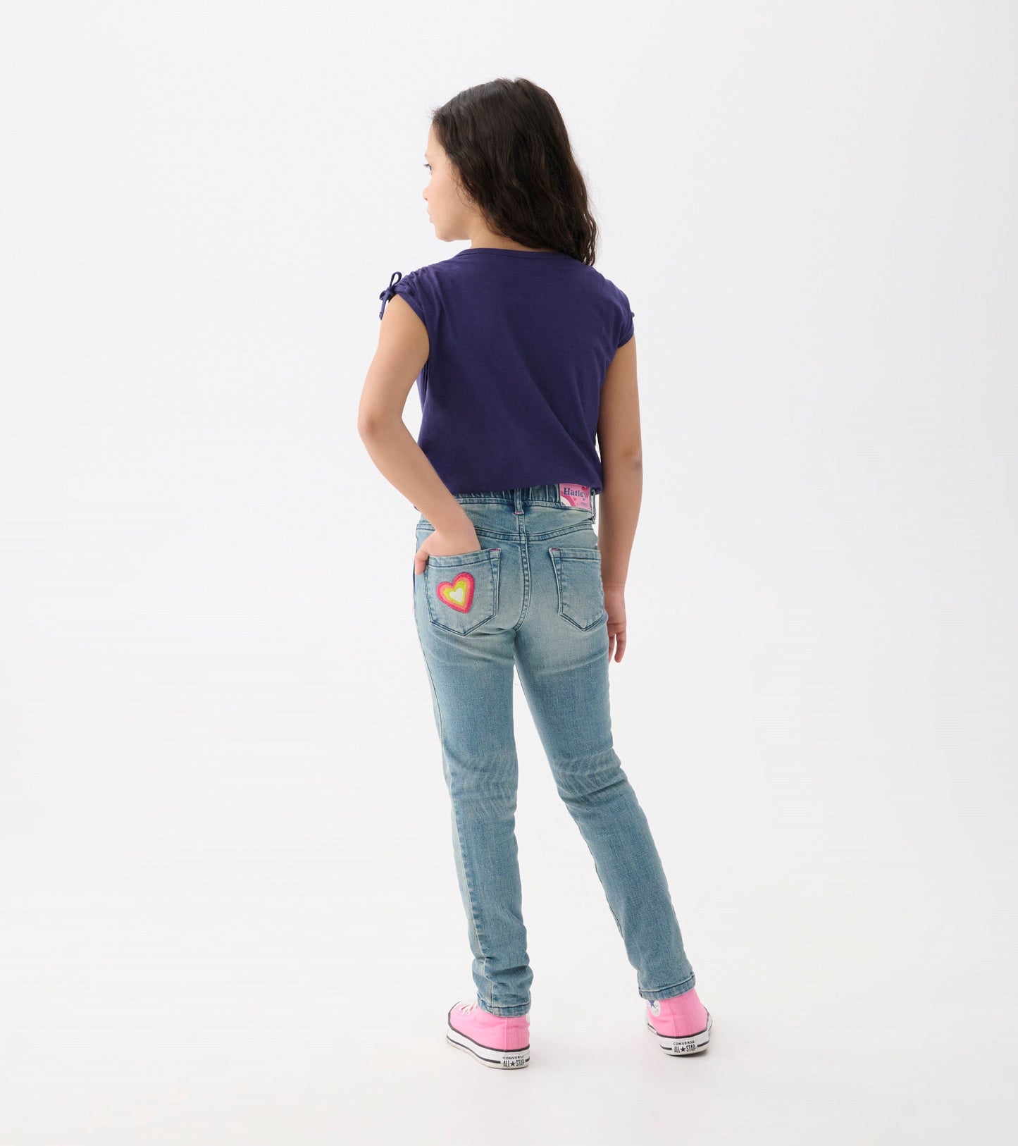Light blue stretch jeans with a heart patch on the back pocket, styled with a purple top and pink shoes.