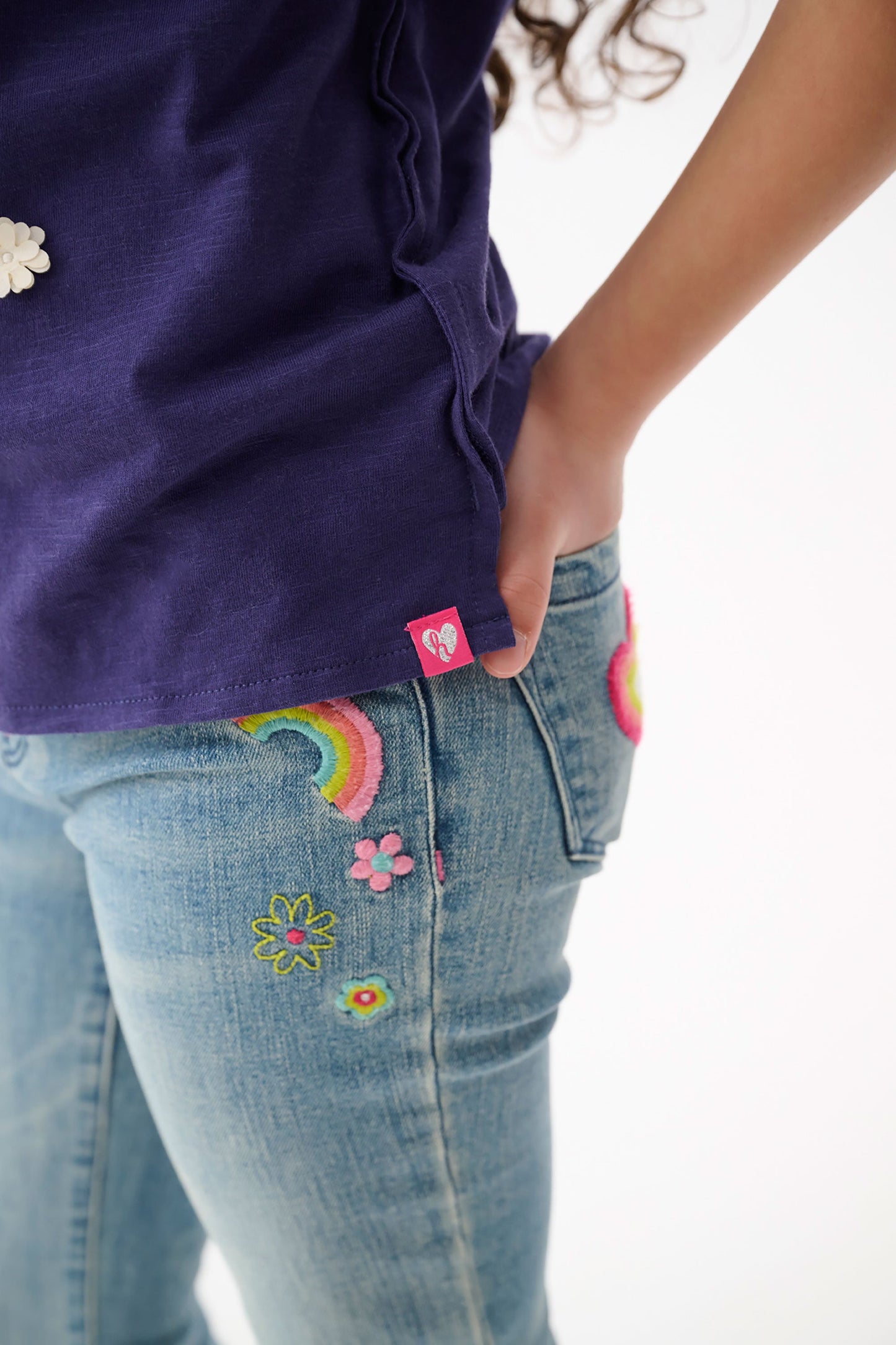 Light blue stretch jeans featuring colorful embroidered patches of flowers and rainbows, shown from the side.