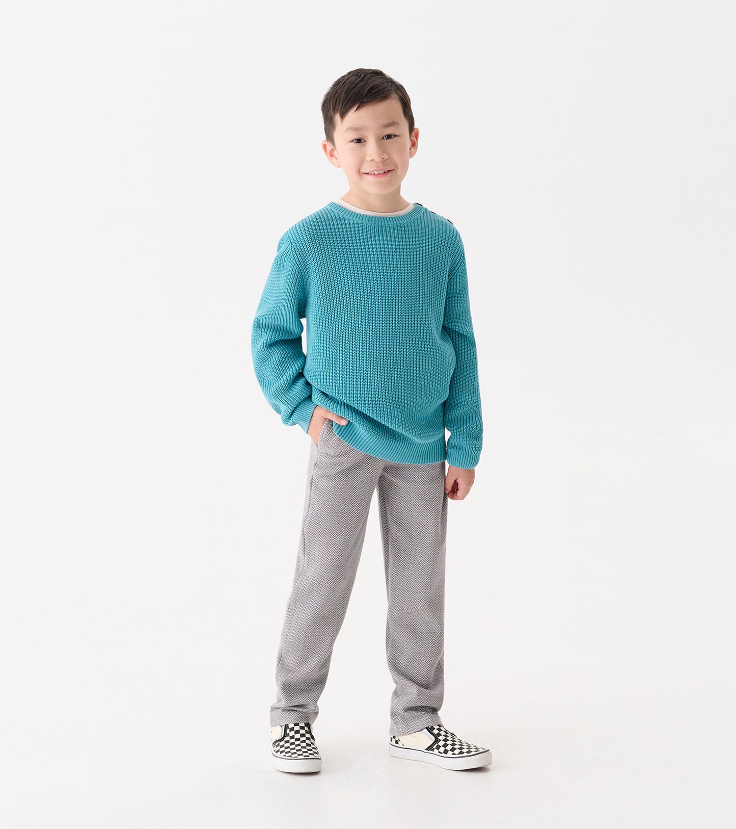 Boys' dark grey herringbone straight leg pants, styled with a turquoise sweater and checkered shoes.