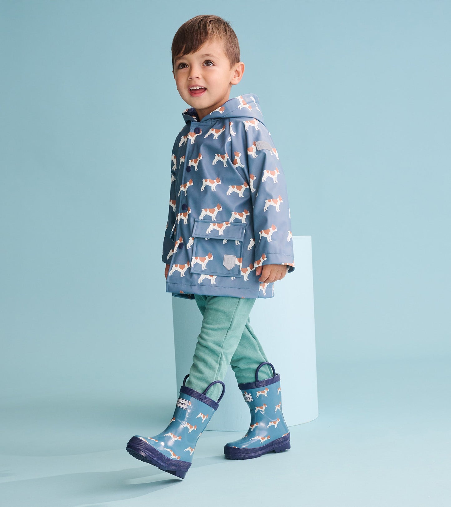 Blue rain jacket featuring French bulldog patterns, paired with green pants and matching blue rain boots.