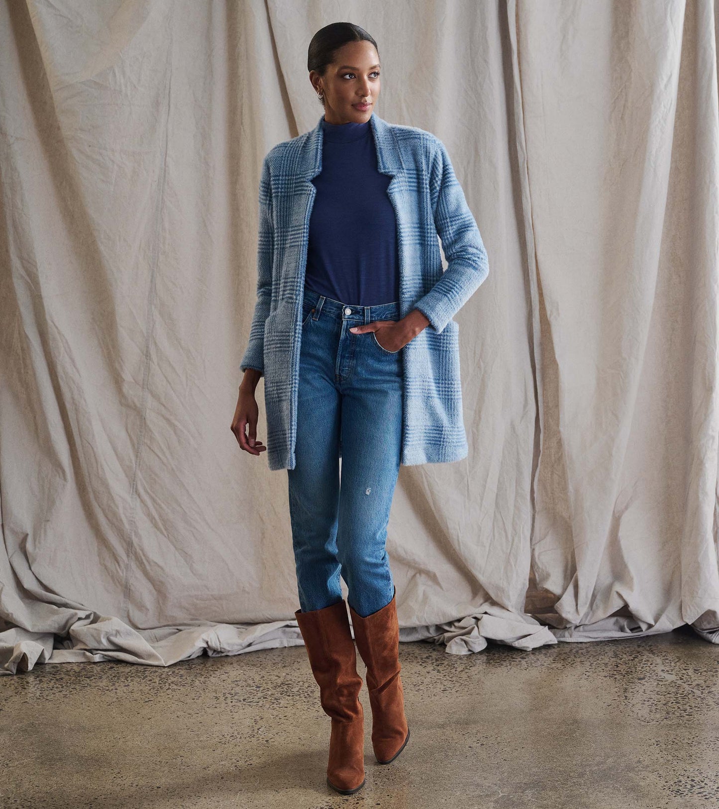 Open front jacket in blue check pattern, paired with a navy top and light jeans, styled with brown knee-high boots.
