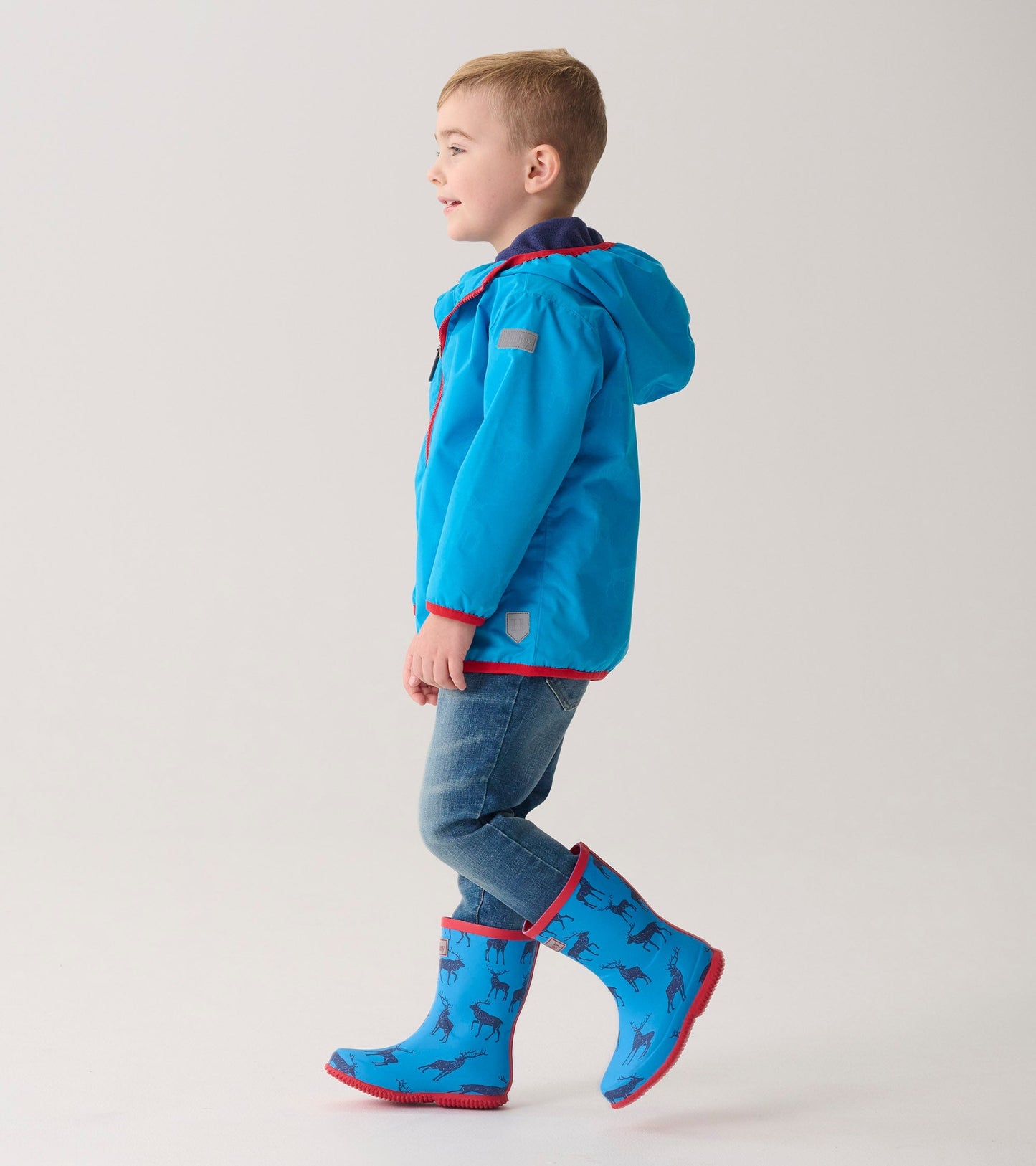 Lightweight blue zip-up rain jacket with red trim, worn by a boy paired with matching blue animal-patterned rain boots.