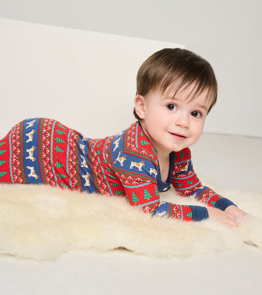Red and blue Fair Isle footed sleeper with dog and tree patterns, worn by a smiling baby on a soft surface.