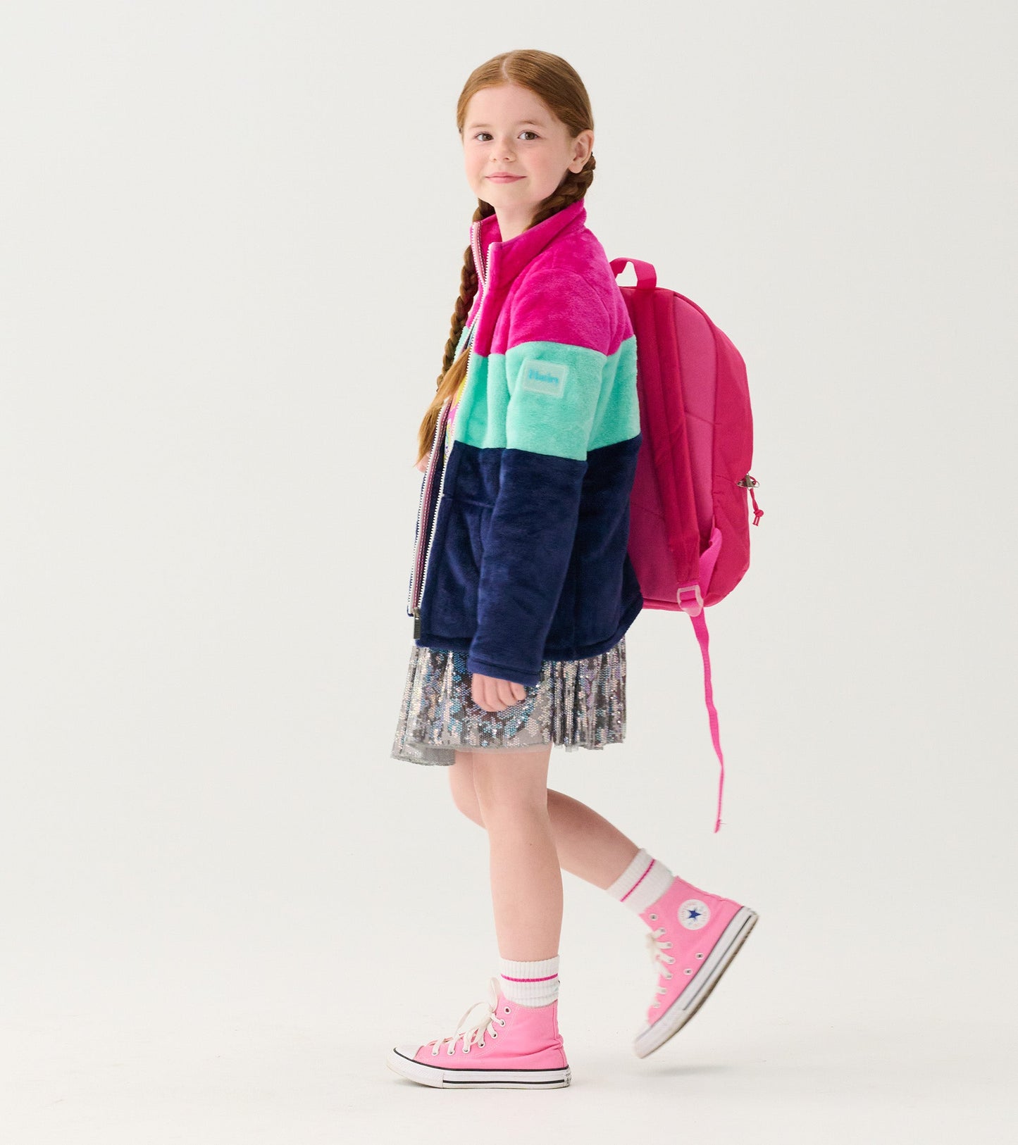 Fuzzy fleece zip-up jacket with colorblock design in pink, teal, and navy, worn by a girl with a pink backpack.