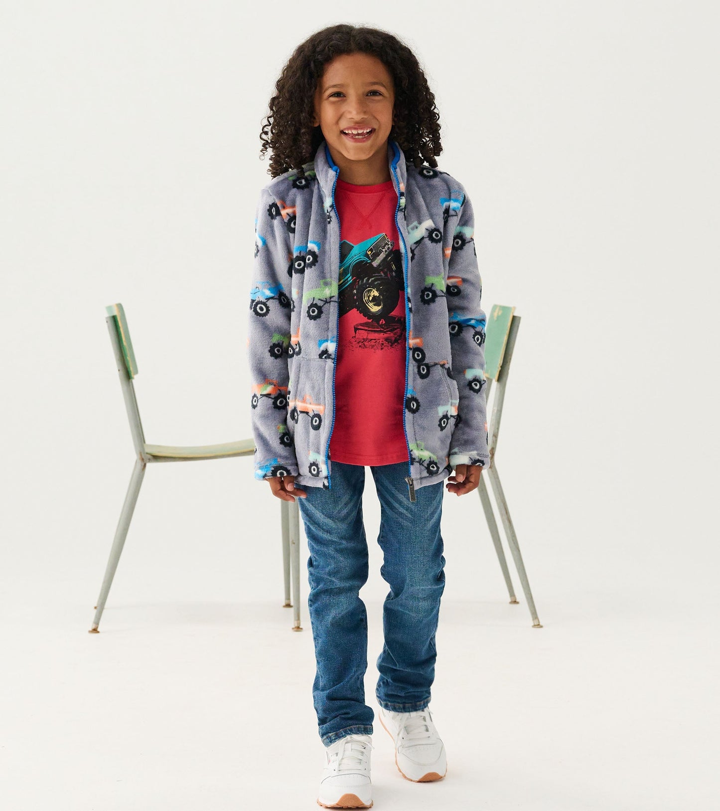 Red long sleeve raglan t-shirt featuring monster truck graphic, paired with blue jeans and white sneakers.