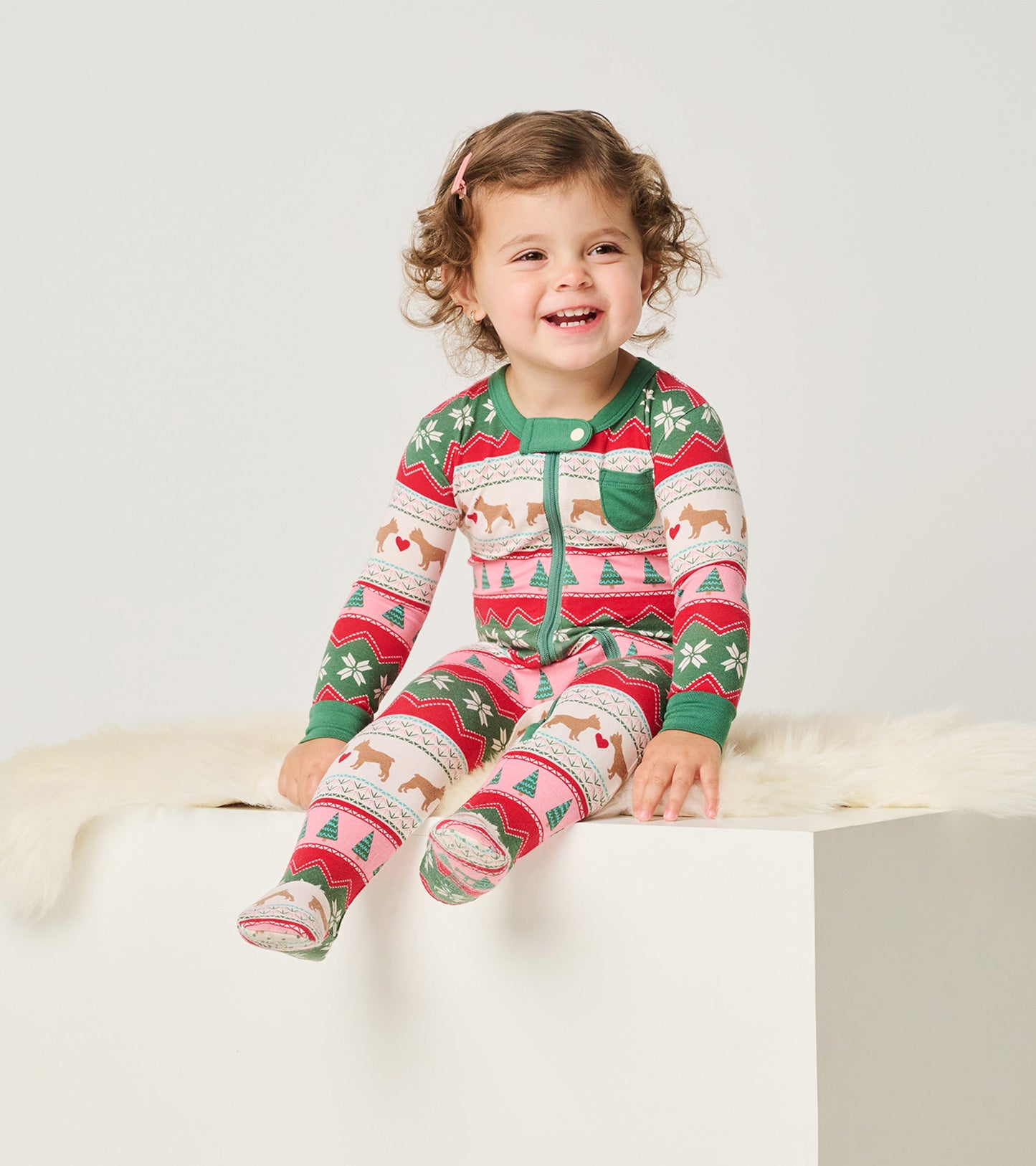 Colorful bamboo footed sleeper with puppy and heart patterns, featuring a green trim and a front pocket, worn by a smiling c…