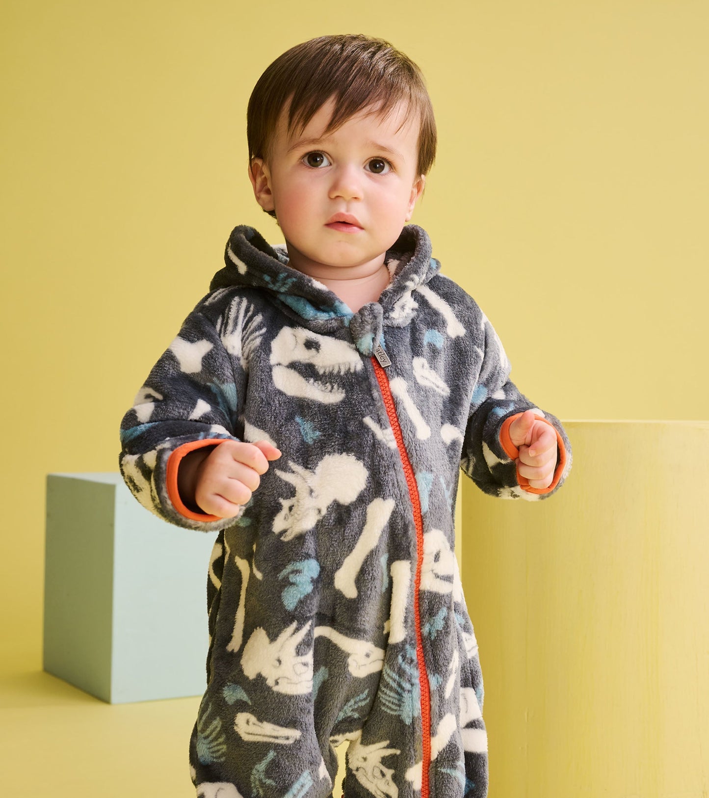Gray fleece suit with dinosaur fossil patterns, featuring a hood and orange zipper, designed for baby boys.