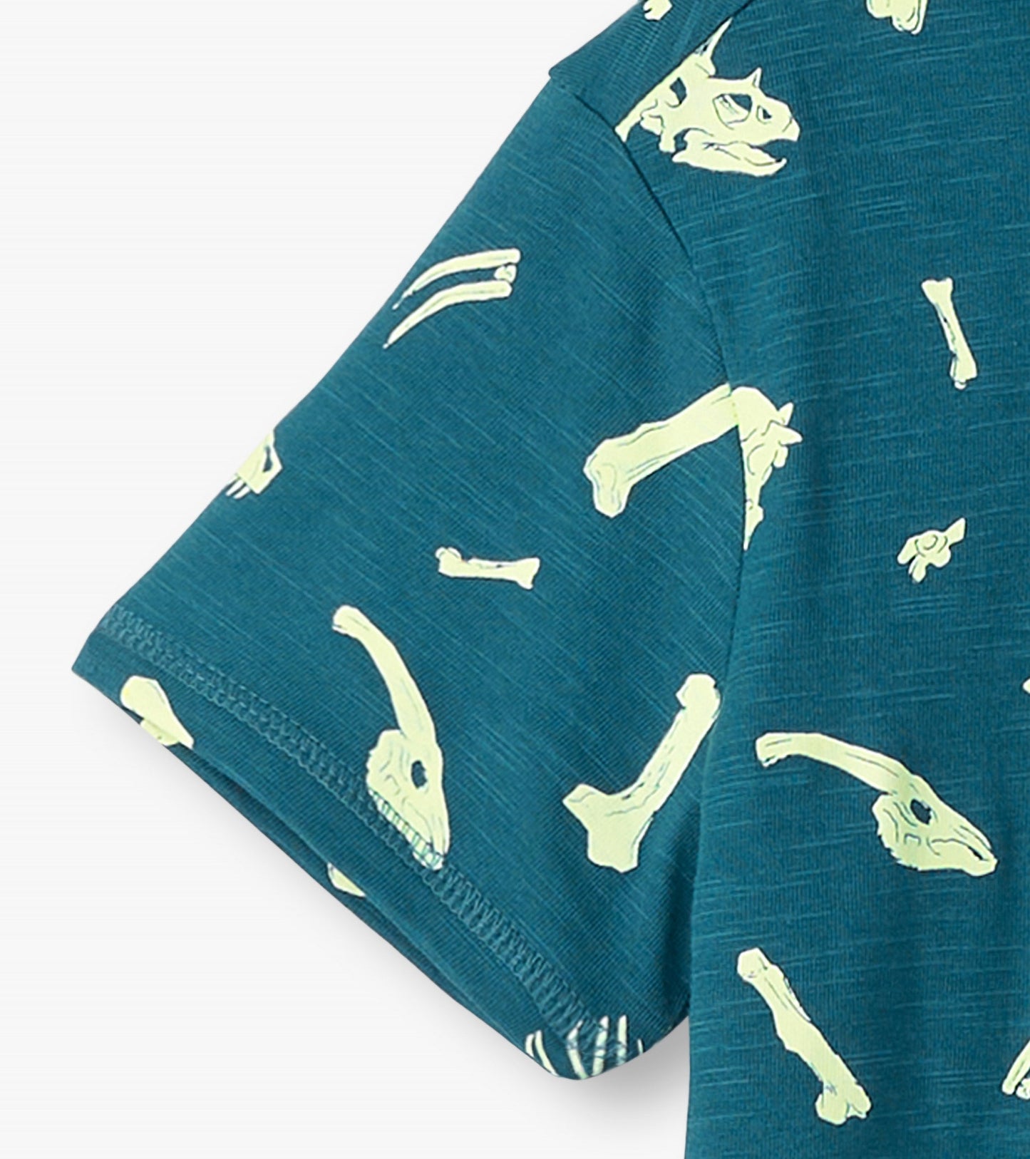 Teal graphic tee featuring glow-in-the-dark dinosaur fossils and bones pattern on soft fabric.