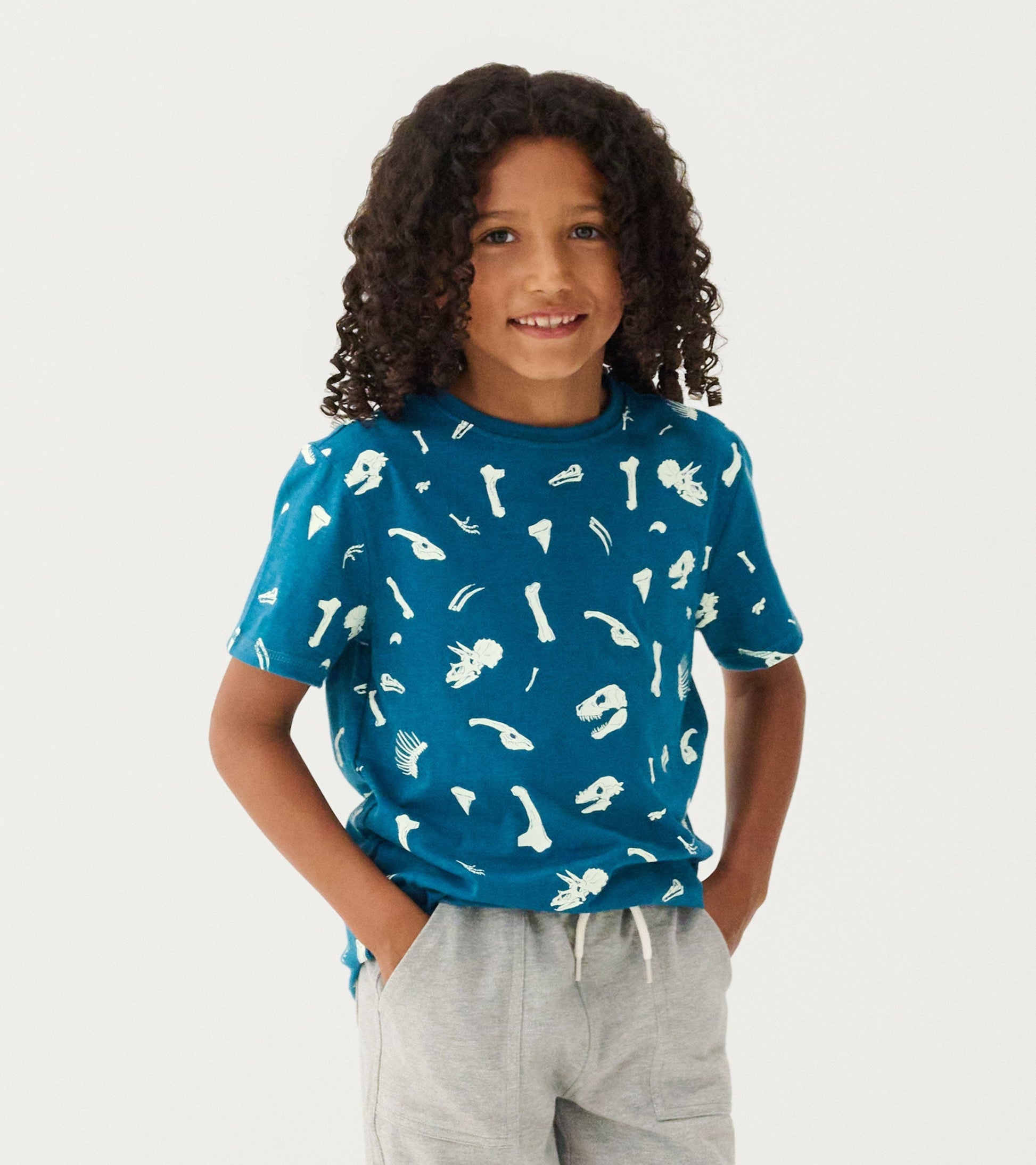 Teal graphic tee featuring glow-in-the-dark dinosaur fossils, short sleeves, and a relaxed fit.