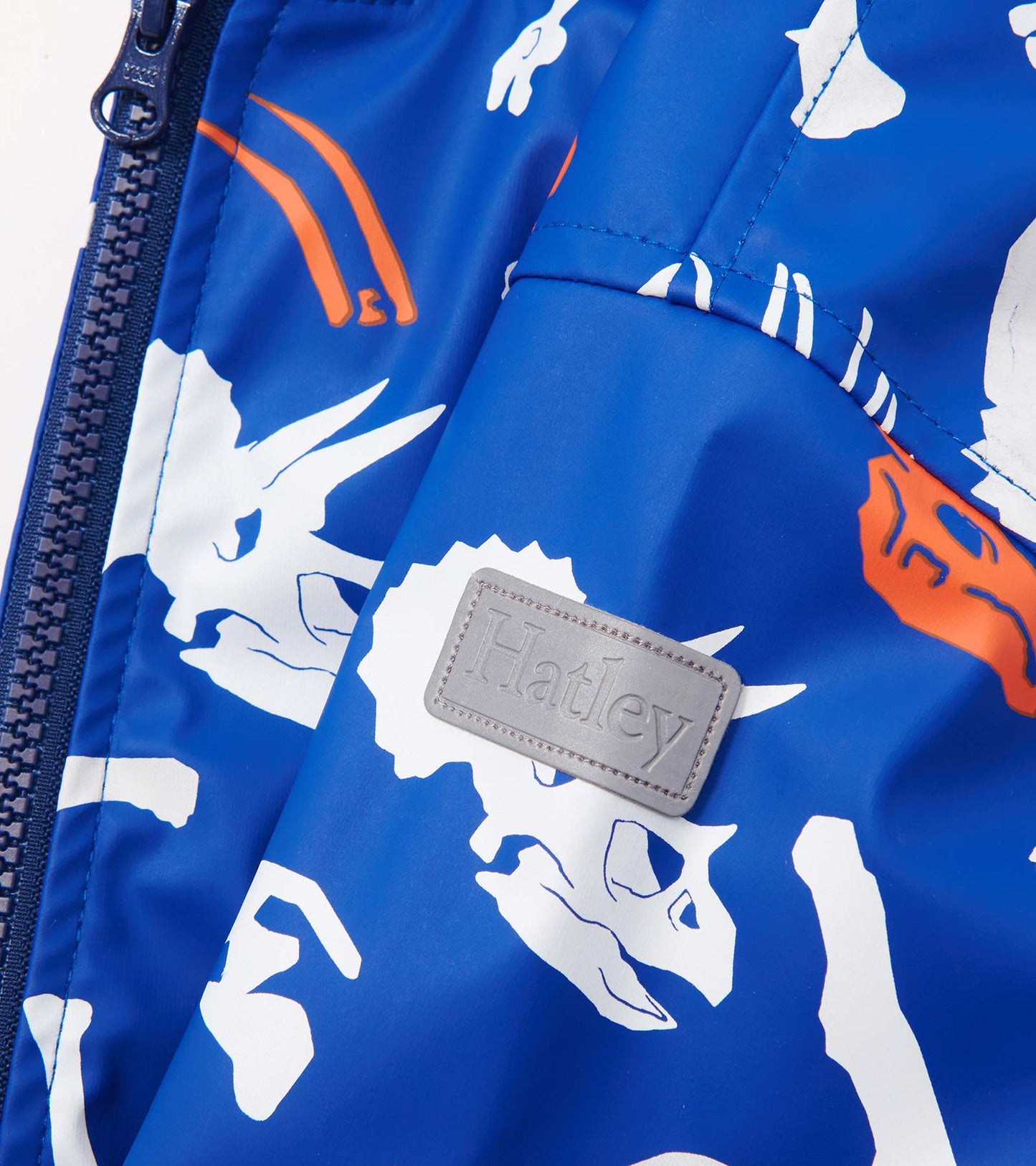 Blue zip-up rain jacket featuring white and orange dinosaur fossil patterns. Ideal for boys, made from waterproof material.
