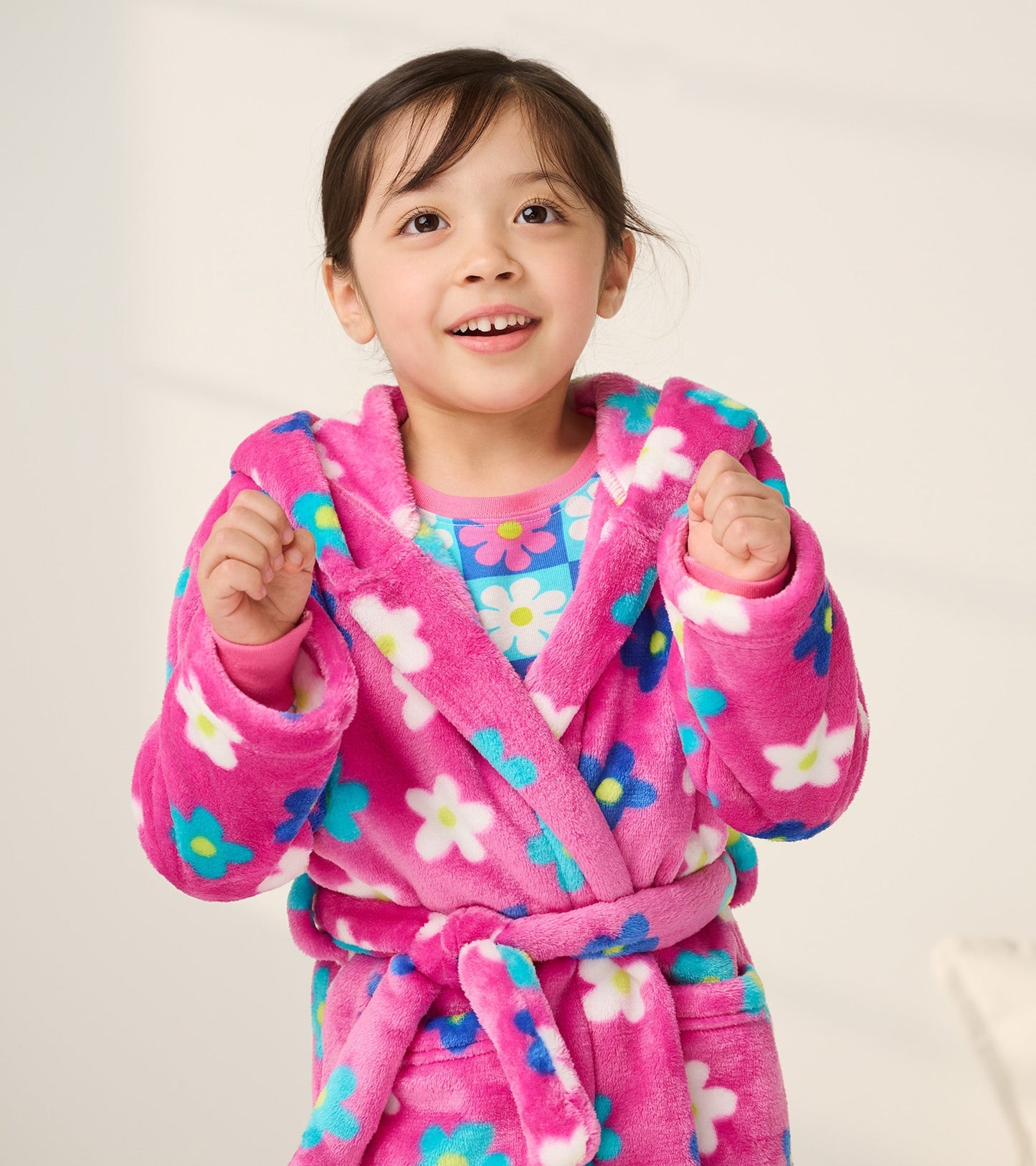 Pink fleece robe with colorful daisy pattern, featuring a hood and belt, worn by a smiling girl.