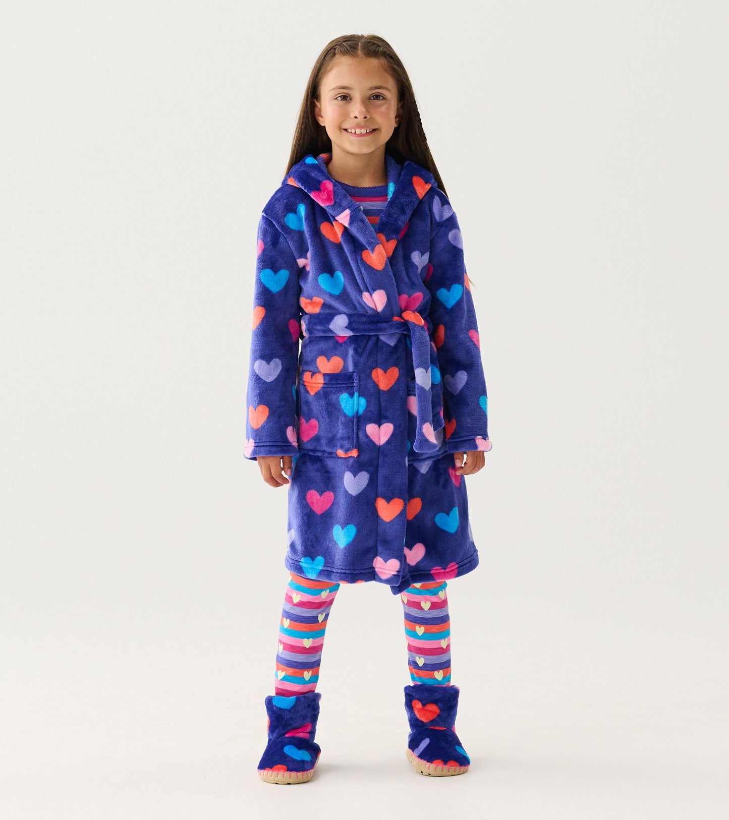 Purple fleece robe with colorful heart patterns, featuring a hood and belt, worn by a girl with striped leggings and slipper…