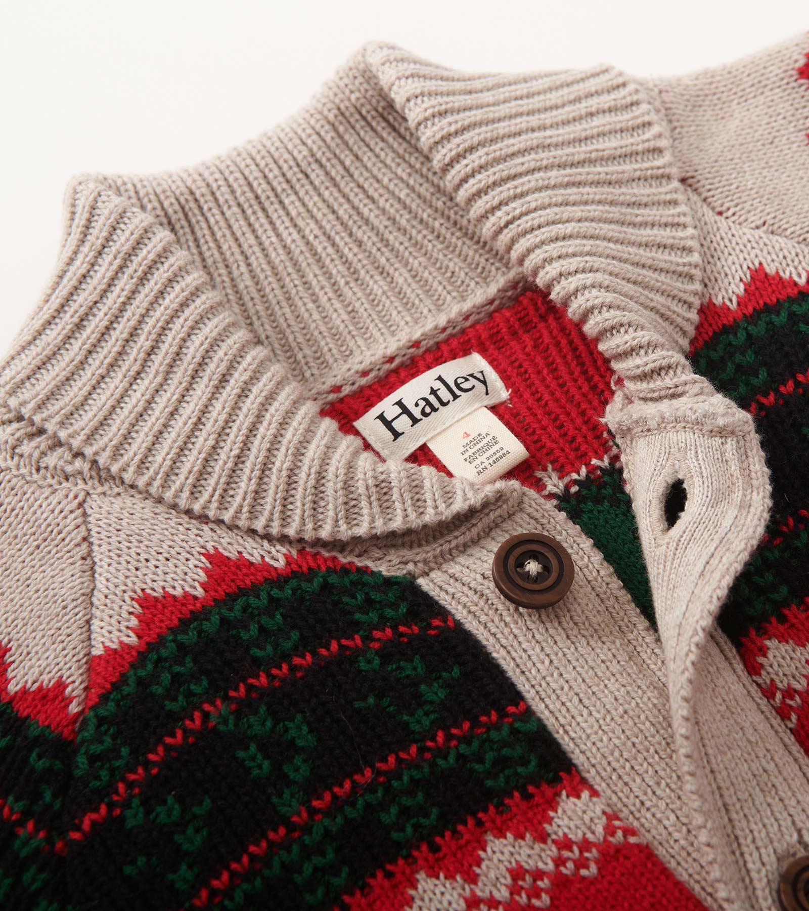 Shawl collar cardigan in beige with red, green, and black patterns, featuring a button closure and ribbed texture.
