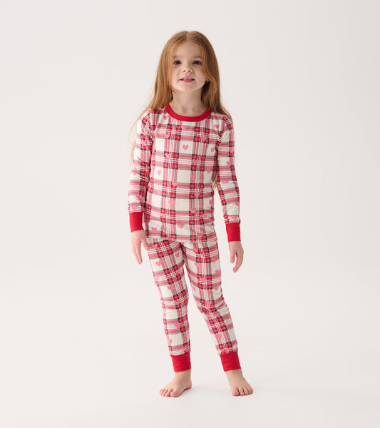 Red and white plaid pajama set with heart patterns, featuring long sleeves and fitted pants, worn by a girl.