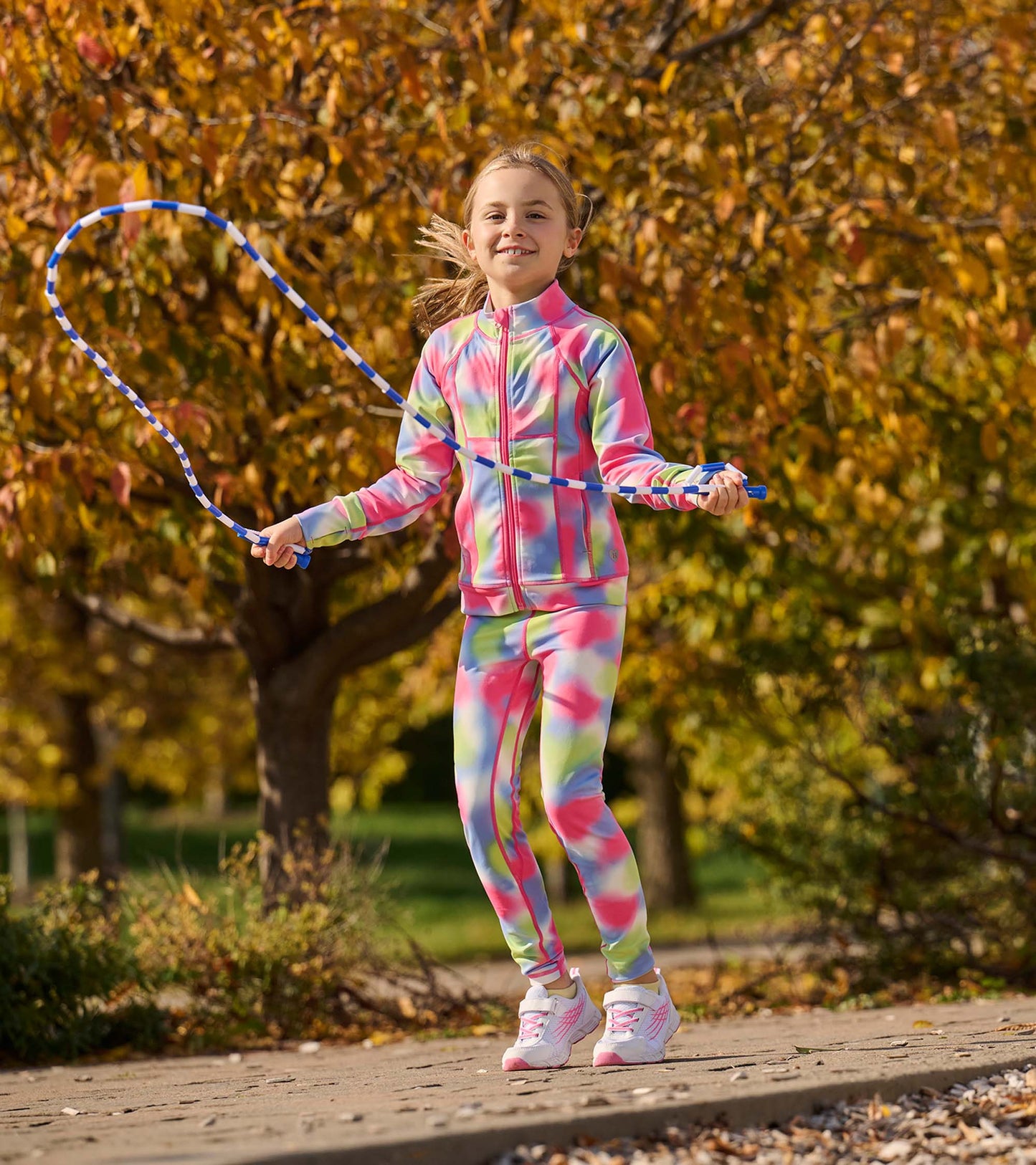 Colorful tie-dye active leggings in pink, green, and yellow, worn by a girl jumping rope outdoors.