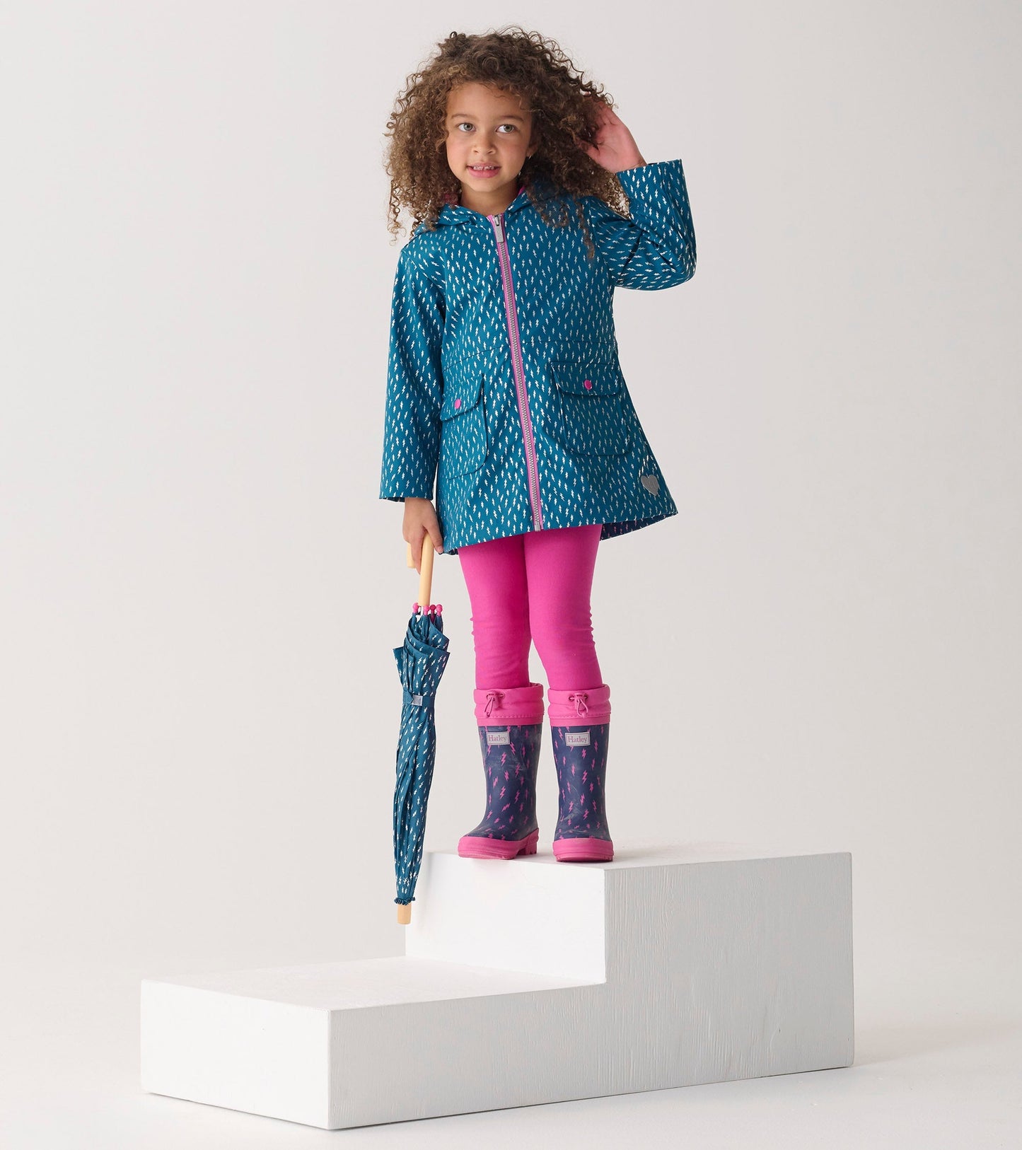 Teal rain jacket with lightning bolt pattern, pink accents, paired with pink leggings and matching umbrella.