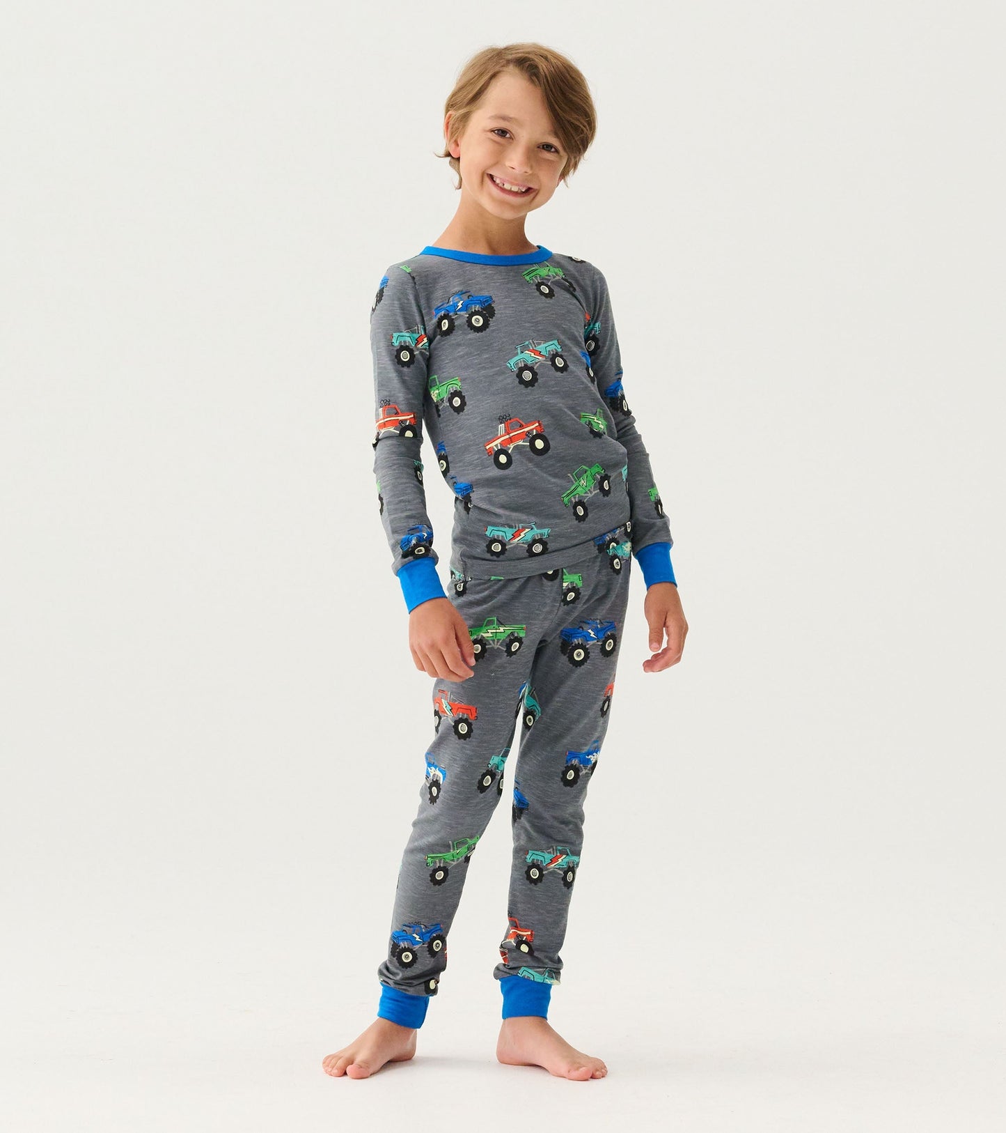 Gray pajama set featuring colorful monster truck prints, with long sleeves and pants, accented by blue cuffs.