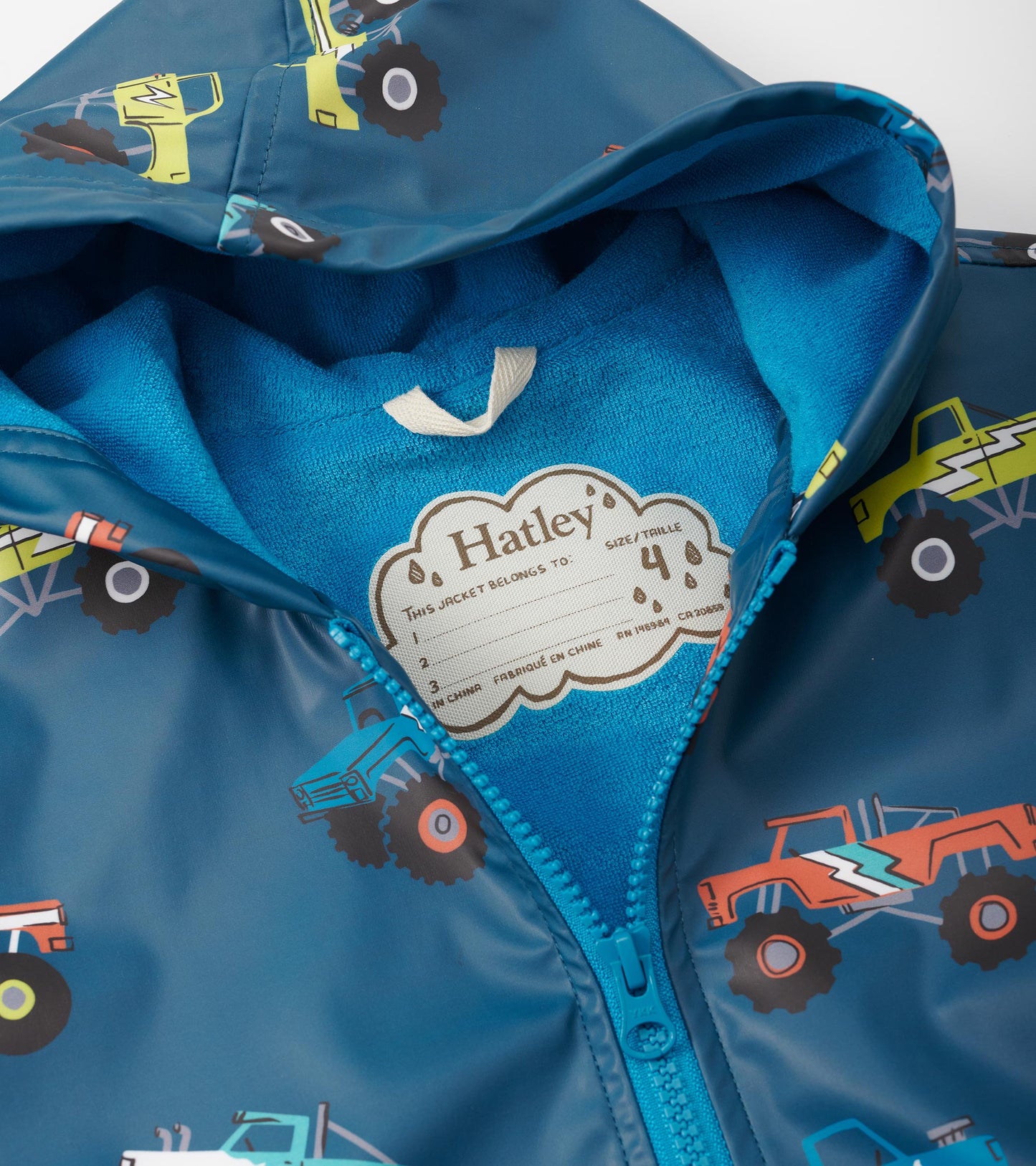 Blue zip-up rain jacket featuring colorful monster truck patterns and a soft inner lining. Size tag visible inside.