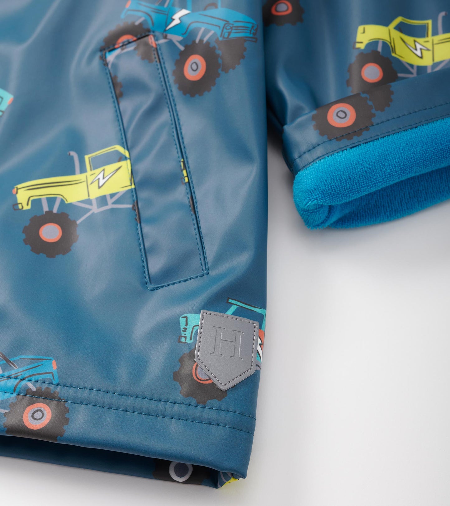 Blue zip-up rain jacket featuring colorful monster truck patterns and a soft, contrasting blue lining.