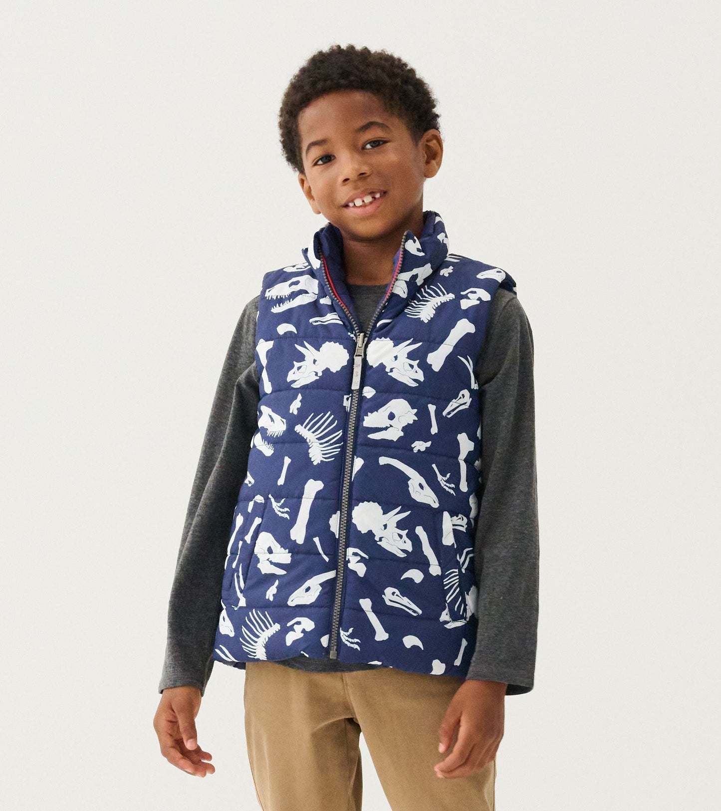 Reversible quilted vest in navy with white dinosaur fossil prints, featuring a zip front and high collar.