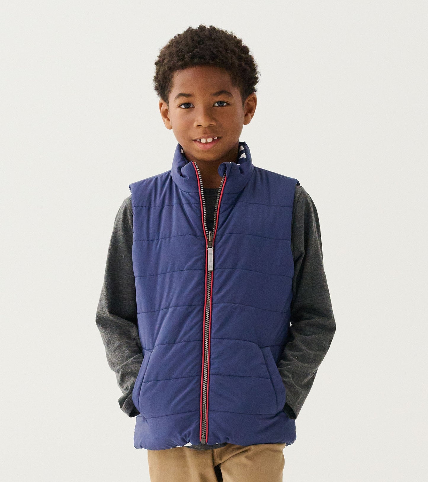 Reversible quilted vest in navy blue with a zip front, featuring a stand collar and side pockets, worn over a gray shirt.