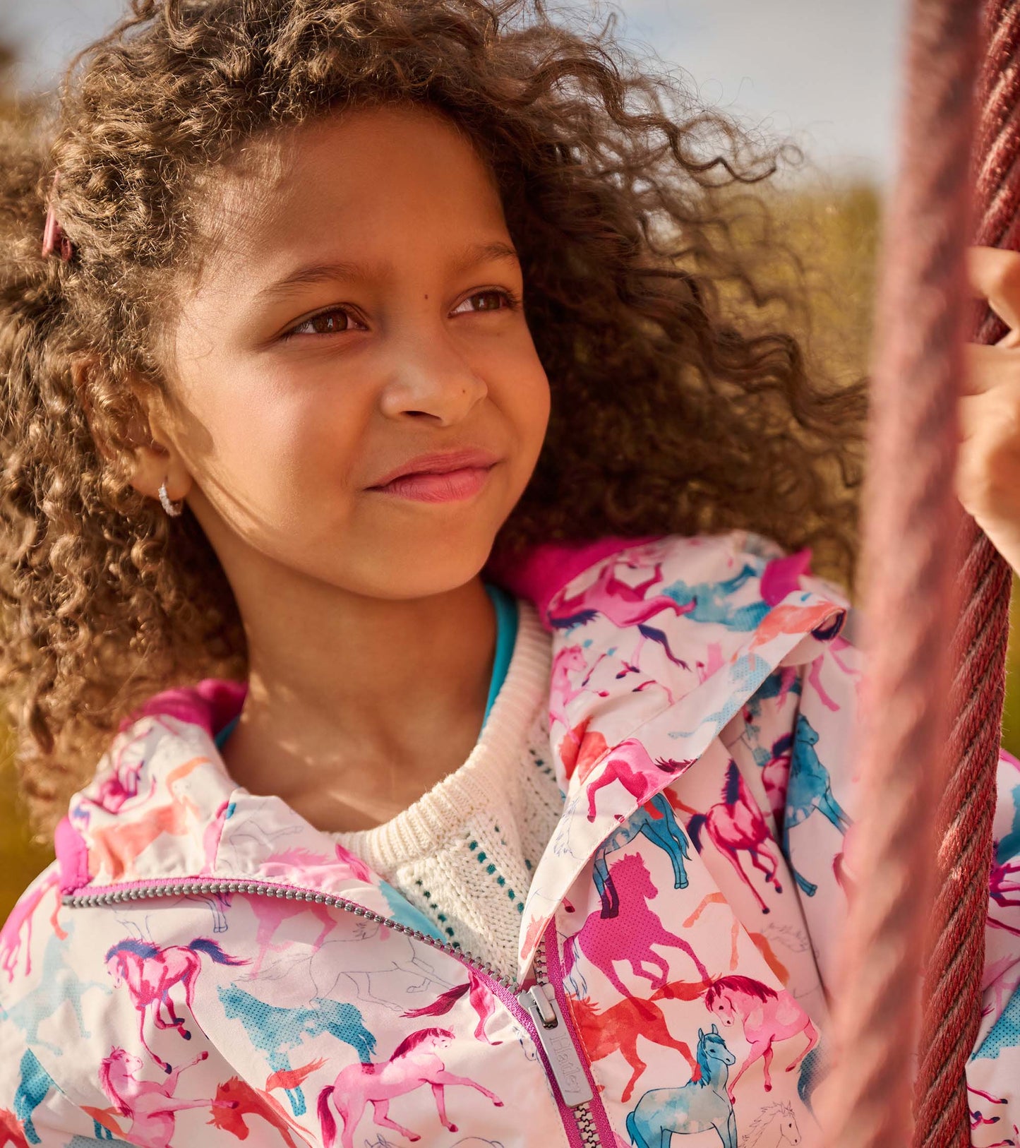Lightweight zip-up rain jacket featuring a colorful horse pattern, ideal for girls, with a pink hood and trim.
