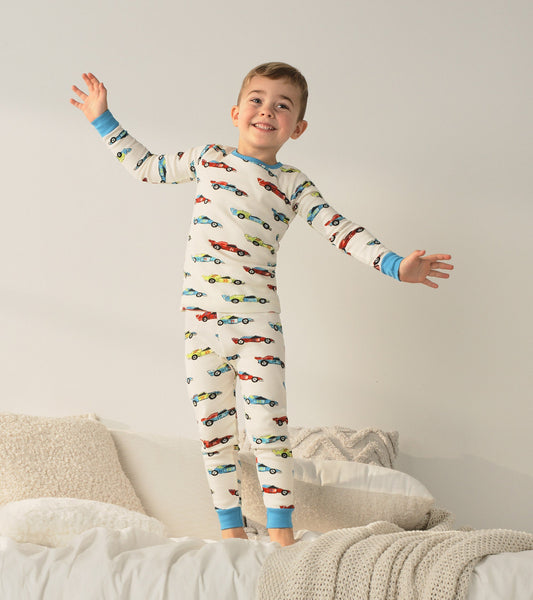 Organic cotton pajama set featuring colorful racecars on a cream background, with blue cuffs and a playful fit for kids.