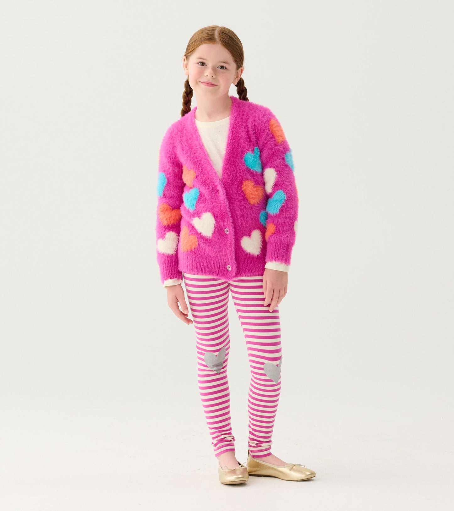 Fuzzy pink cardigan with colorful heart patterns, paired with striped leggings and gold flats.