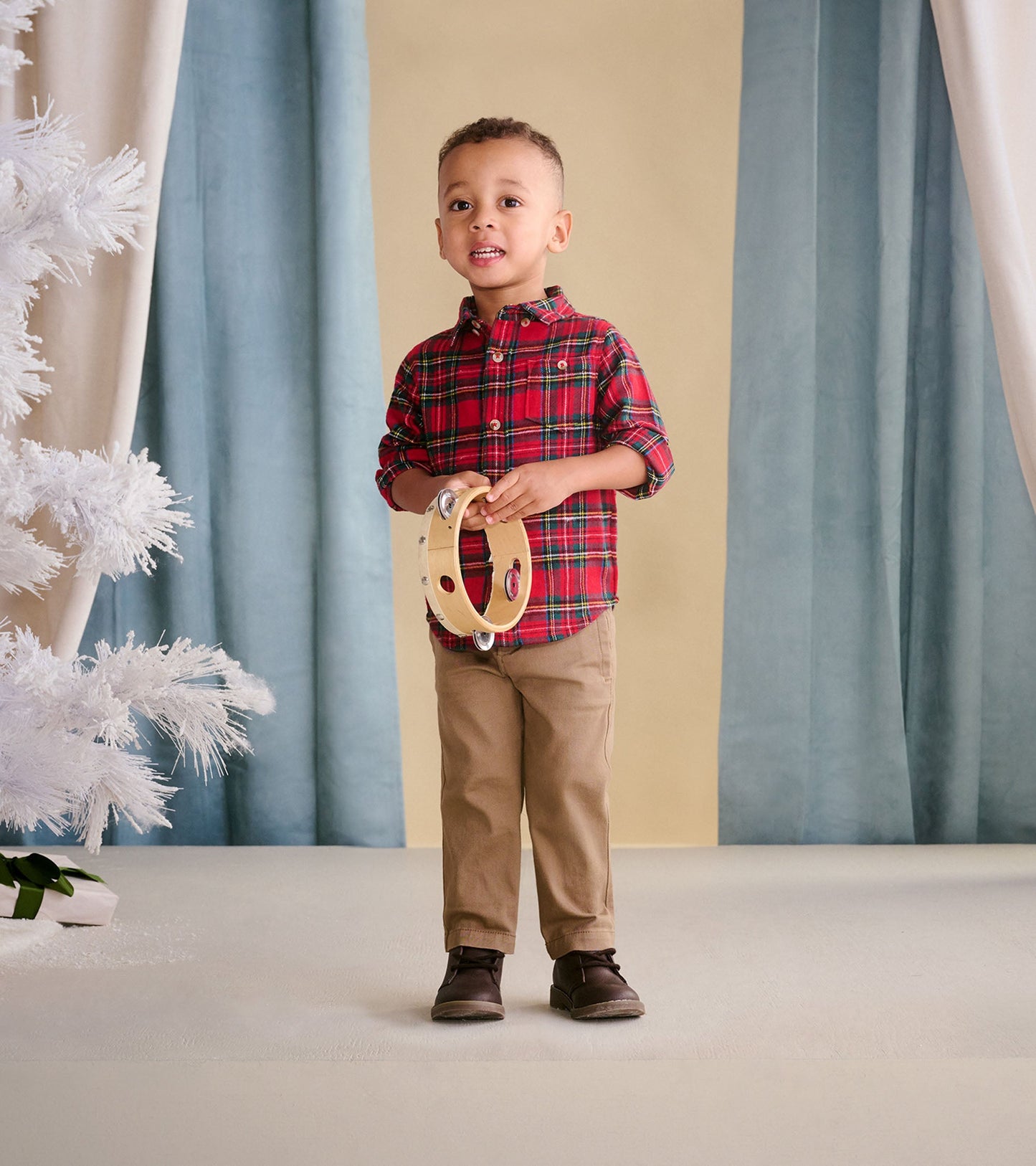 Red plaid button-down shirt for babies and toddlers, styled with khaki pants and holding a tambourine.