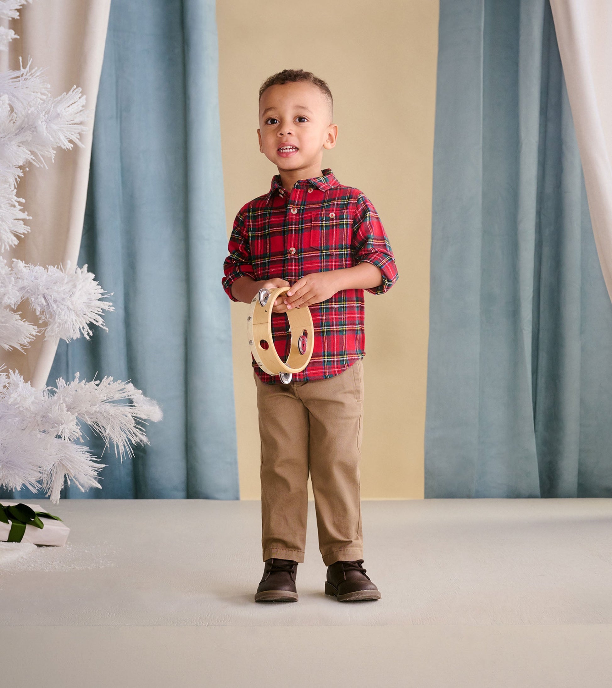 Red plaid button-down shirt for babies and toddlers, styled with khaki pants and holding a tambourine.