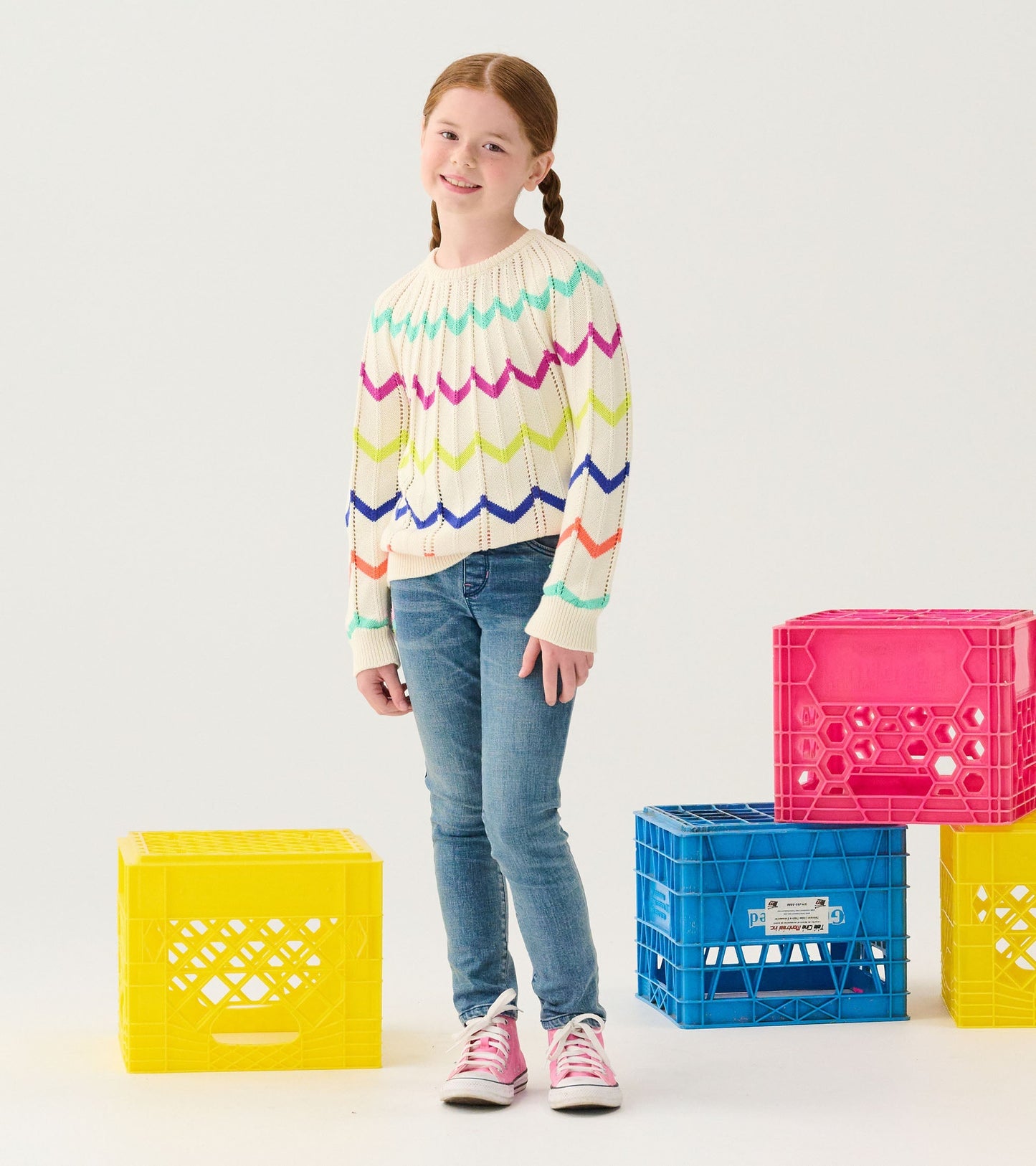 Cream sweater with colorful zigzag pattern, long sleeves, worn with blue jeans and pink sneakers.