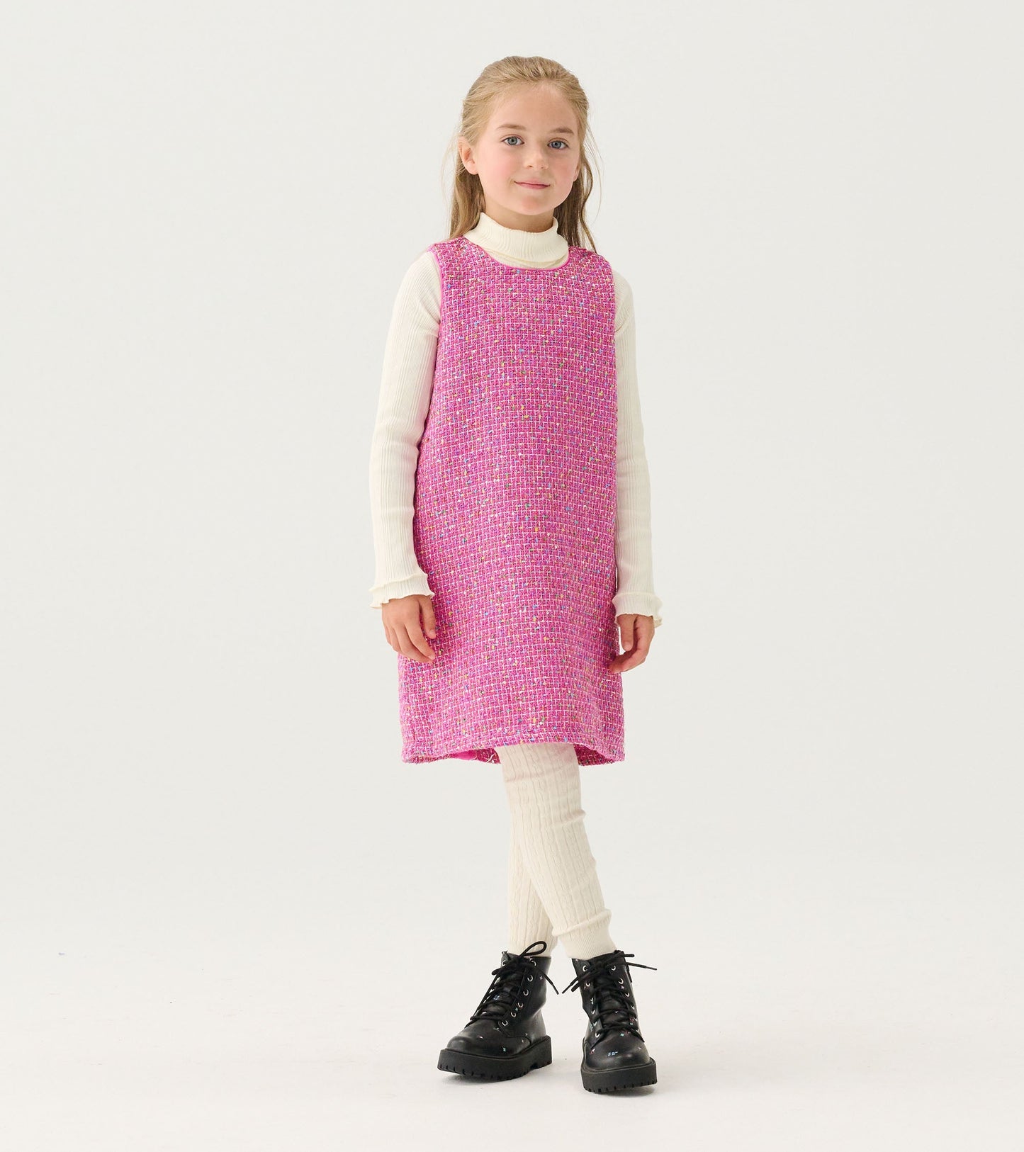 Pink tweed dress with a relaxed fit, worn over a white turtleneck, paired with ribbed leggings and black boots.