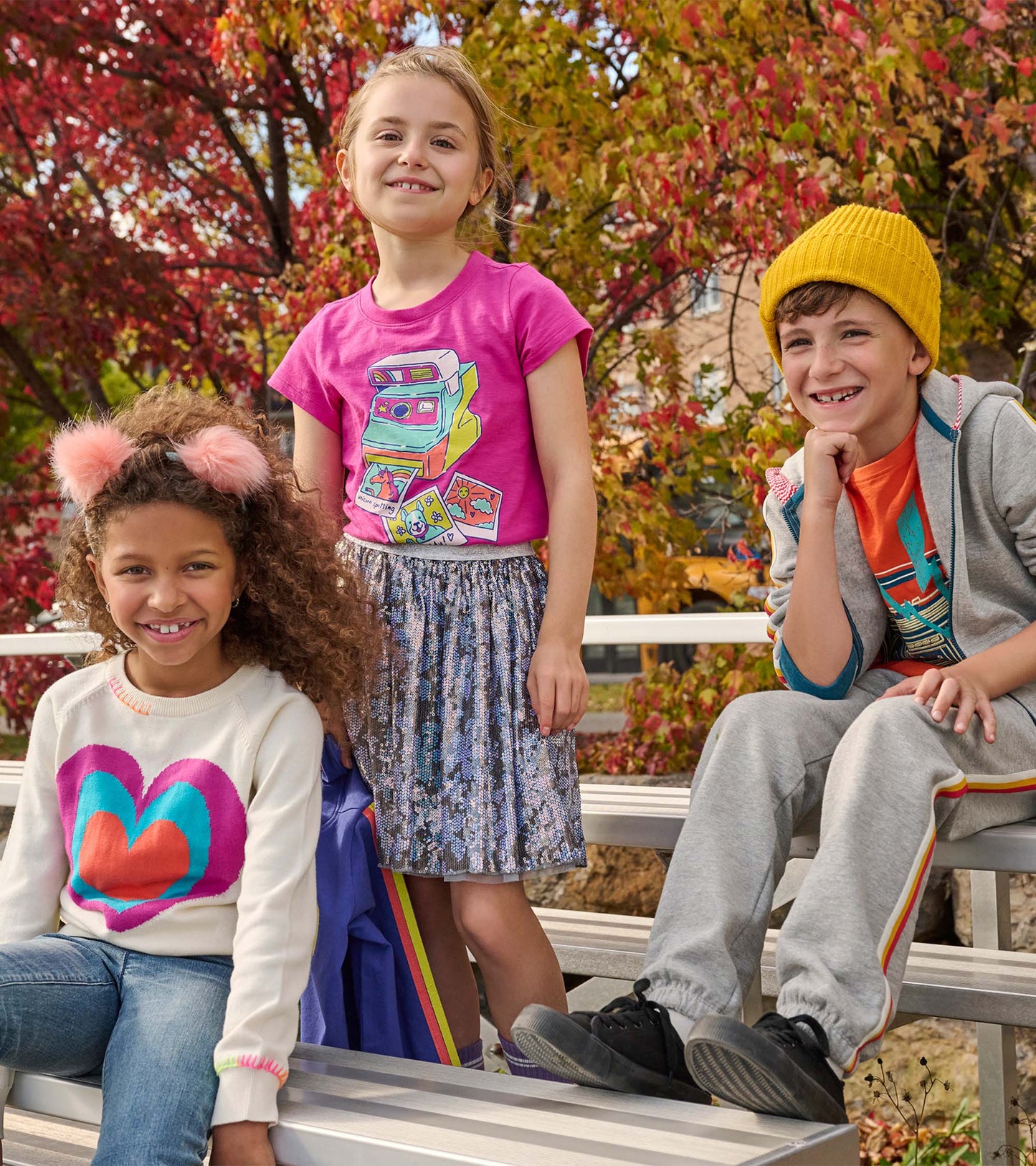 Pink graphic tee featuring a colorful retro camera design, paired with a sparkly skirt, worn by a smiling girl.