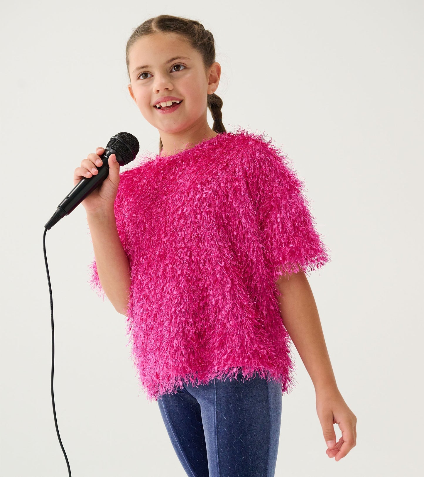 Fluffy pink knit sweater with short sleeves, worn by a girl holding a microphone, paired with dark blue jeans.