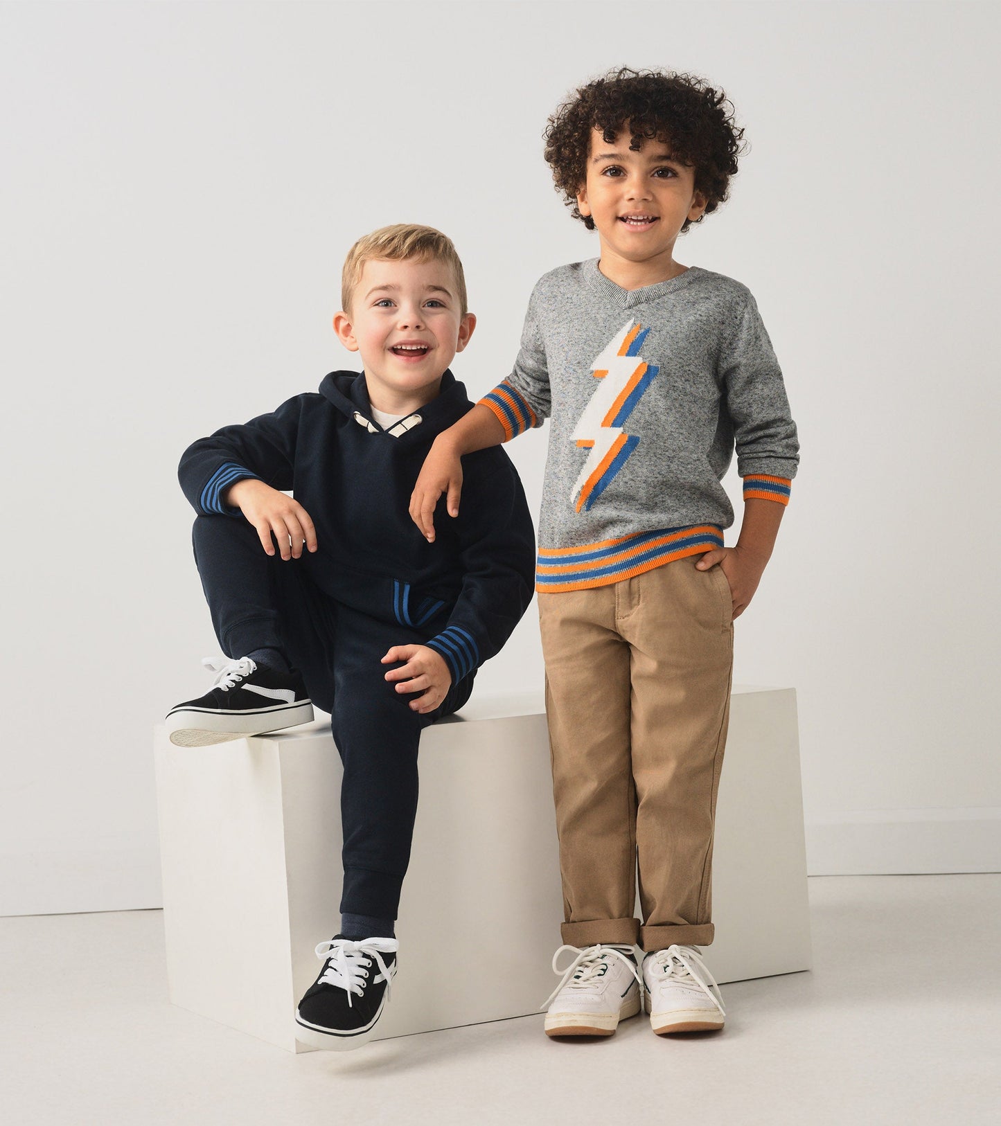 Gray pullover with a lightning bolt design, paired with beige pants, worn by two smiling boys.