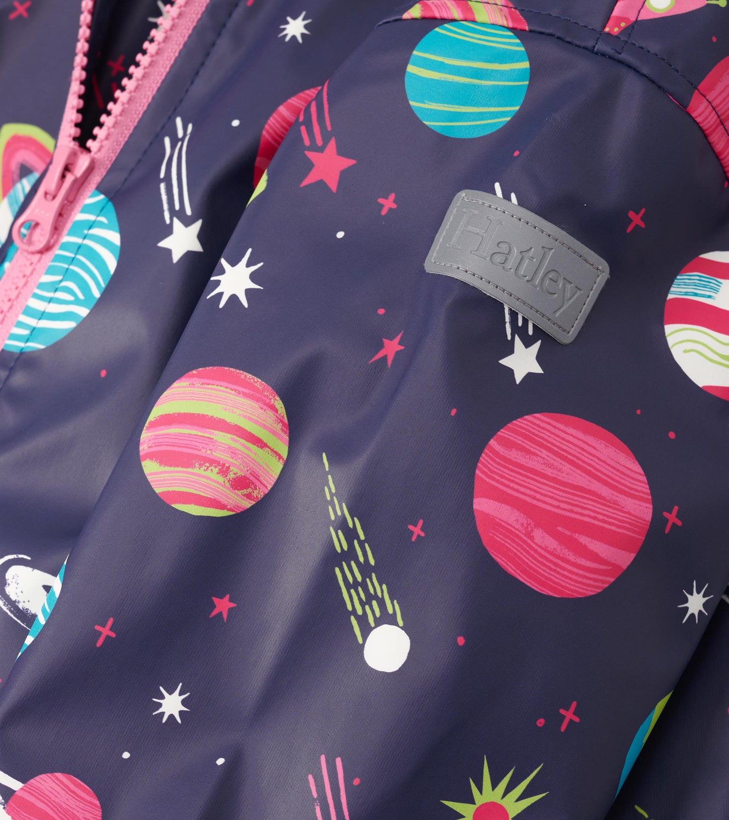 Navy rain jacket featuring colorful planet and star patterns, with a pink zipper and logo patch. Ideal for wet weather.