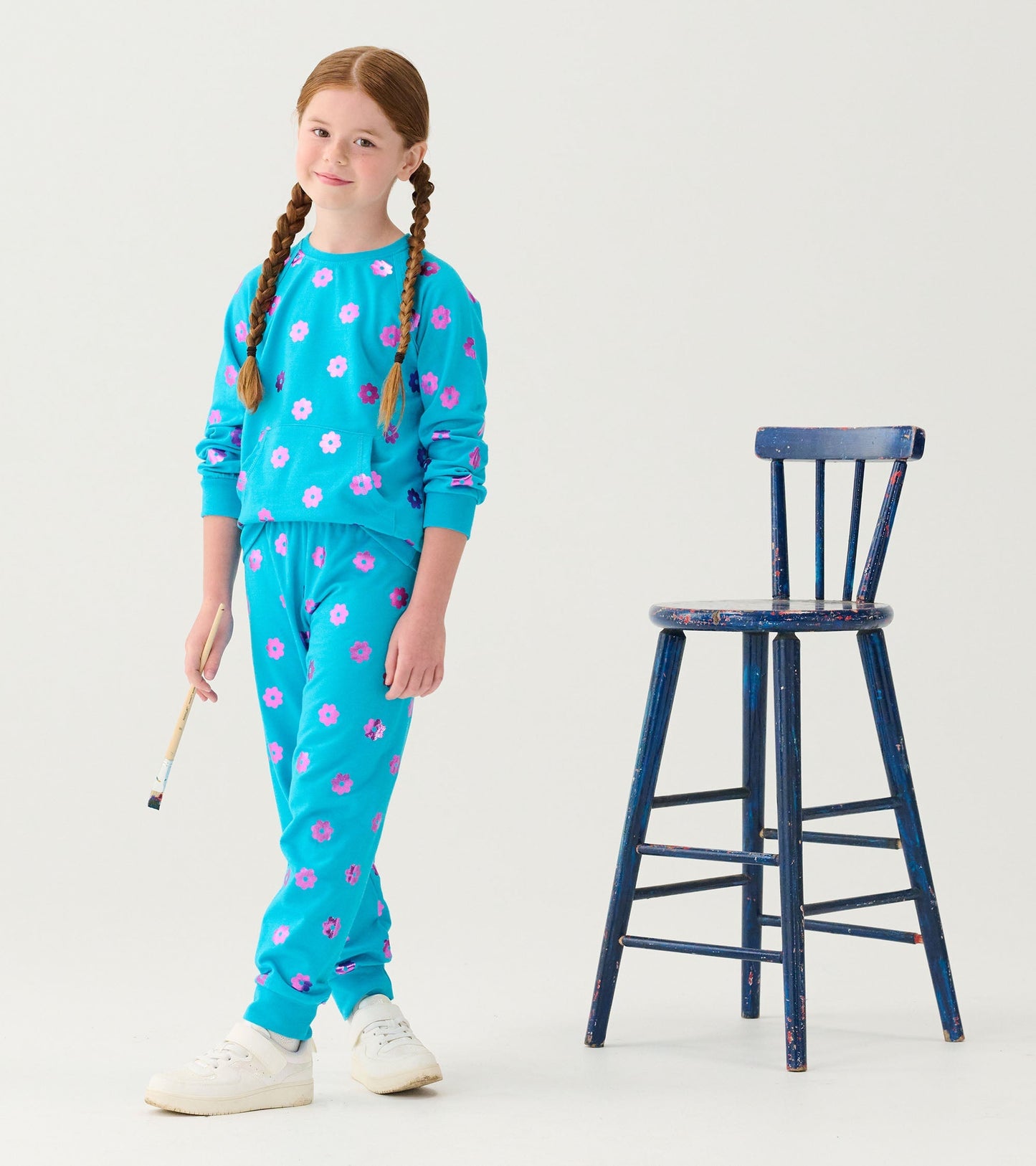 Turquoise sweater with pink and purple floral pattern, paired with matching pants, worn by a girl holding a paintbrush.