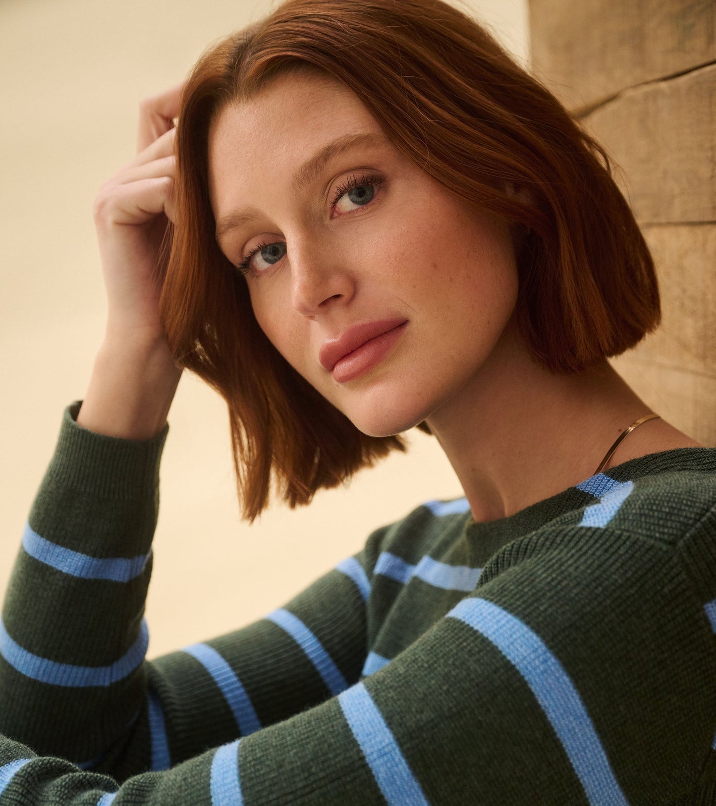 Teal heather sweater featuring blue stripes, round neckline, and long sleeves, styled casually against a wooden backdrop.