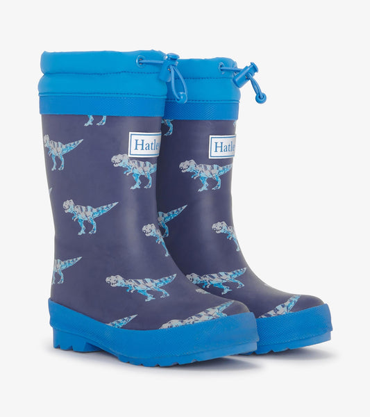 Blue and navy rain boots featuring a T-Rex pattern, with a sherpa lining and adjustable top for a secure fit.
