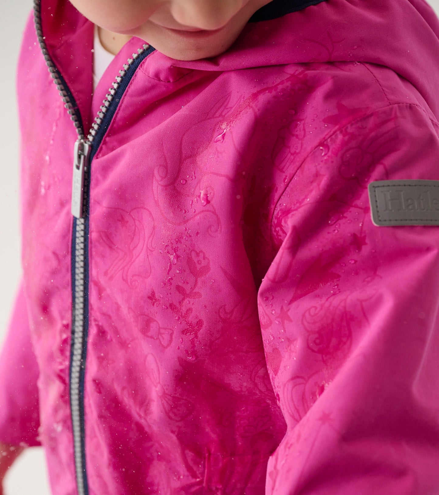 Lightweight pink zip-up rain jacket featuring a unicorn doodle pattern and a hood, suitable for girls.