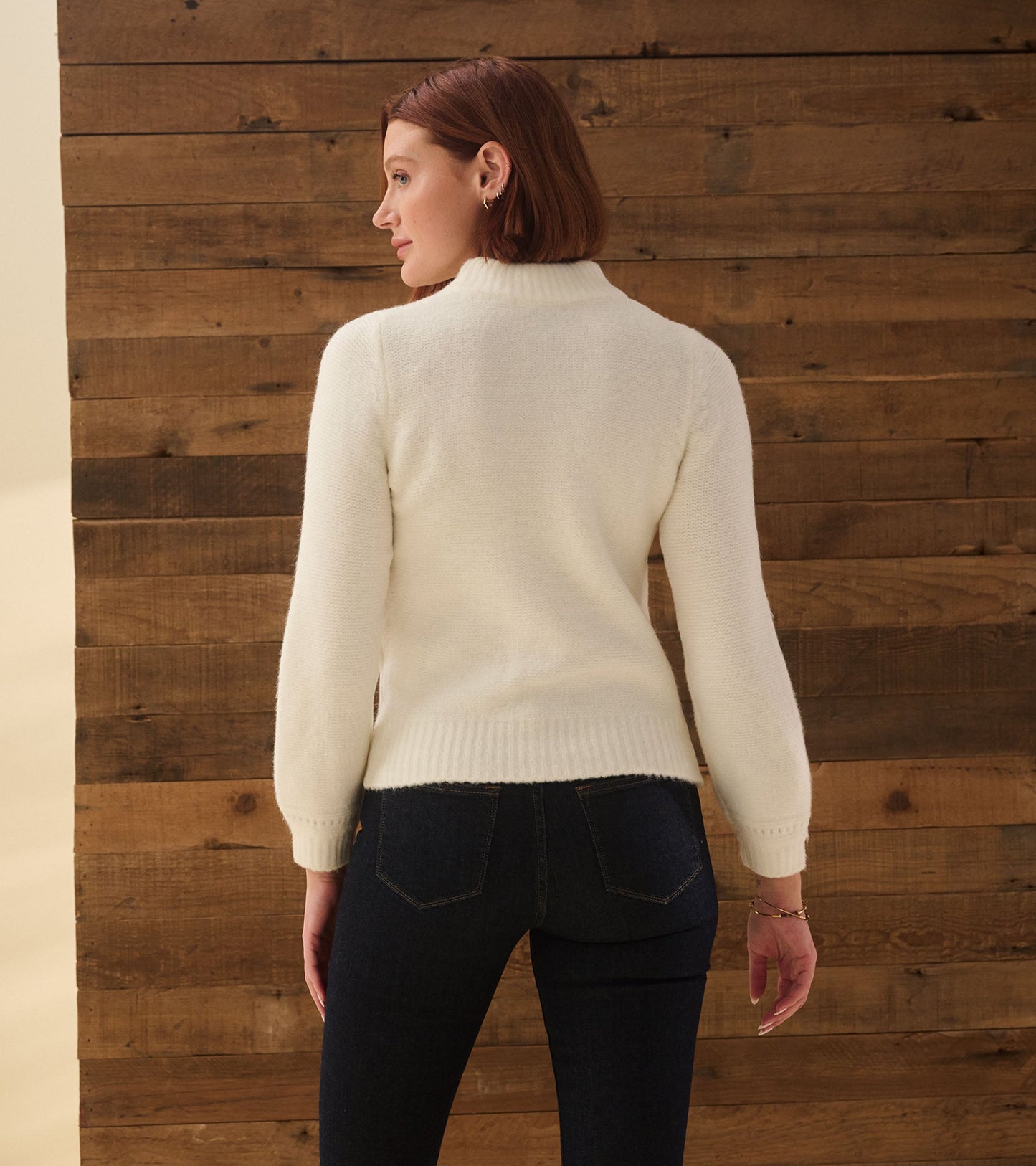 Winter white cable sweater with a high neck and balloon sleeves, styled with dark jeans against a wooden backdrop.