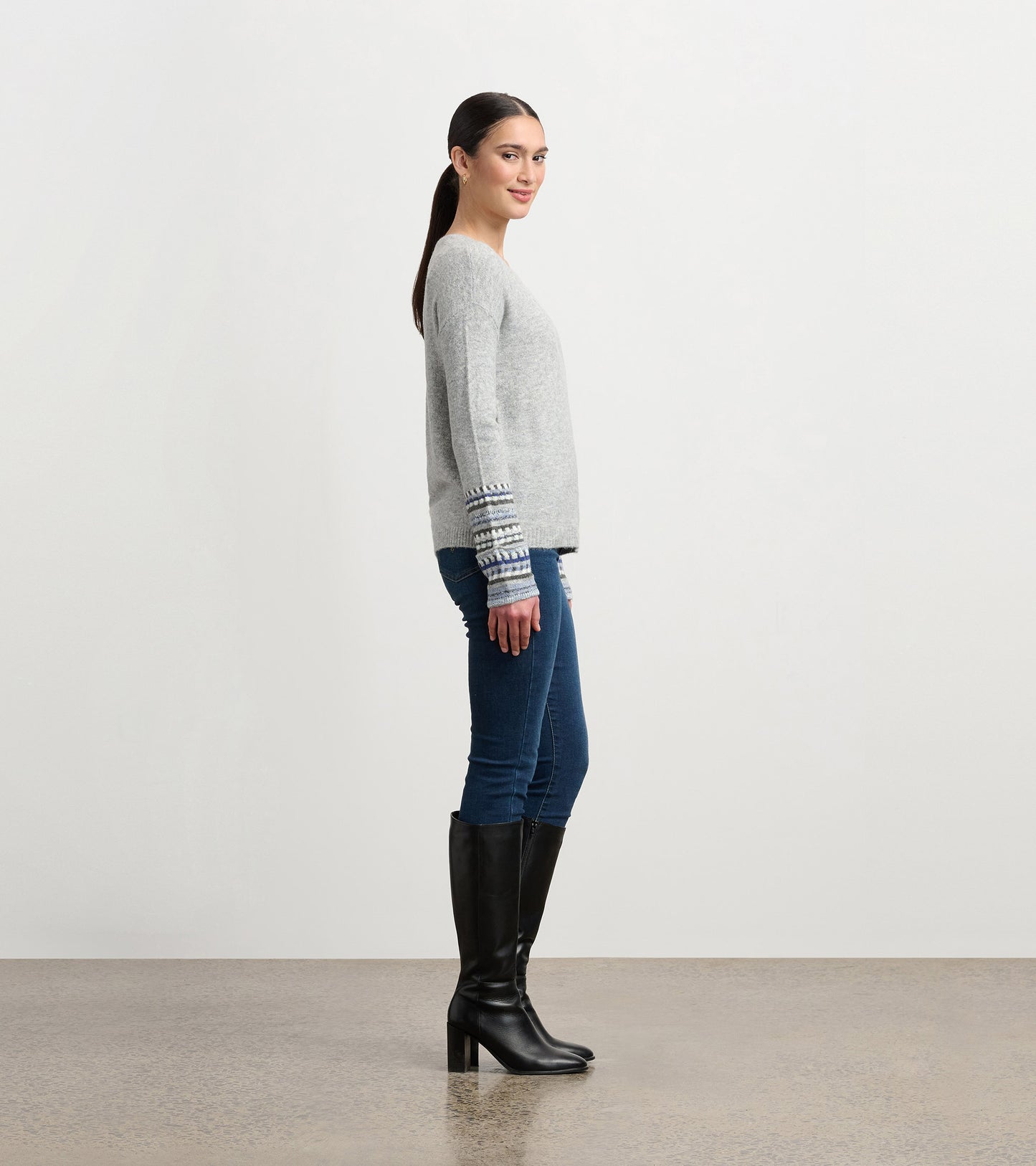 Grey melange sweater with patterned cuffs, featuring a relaxed fit, styled with blue jeans and knee-high black boots.