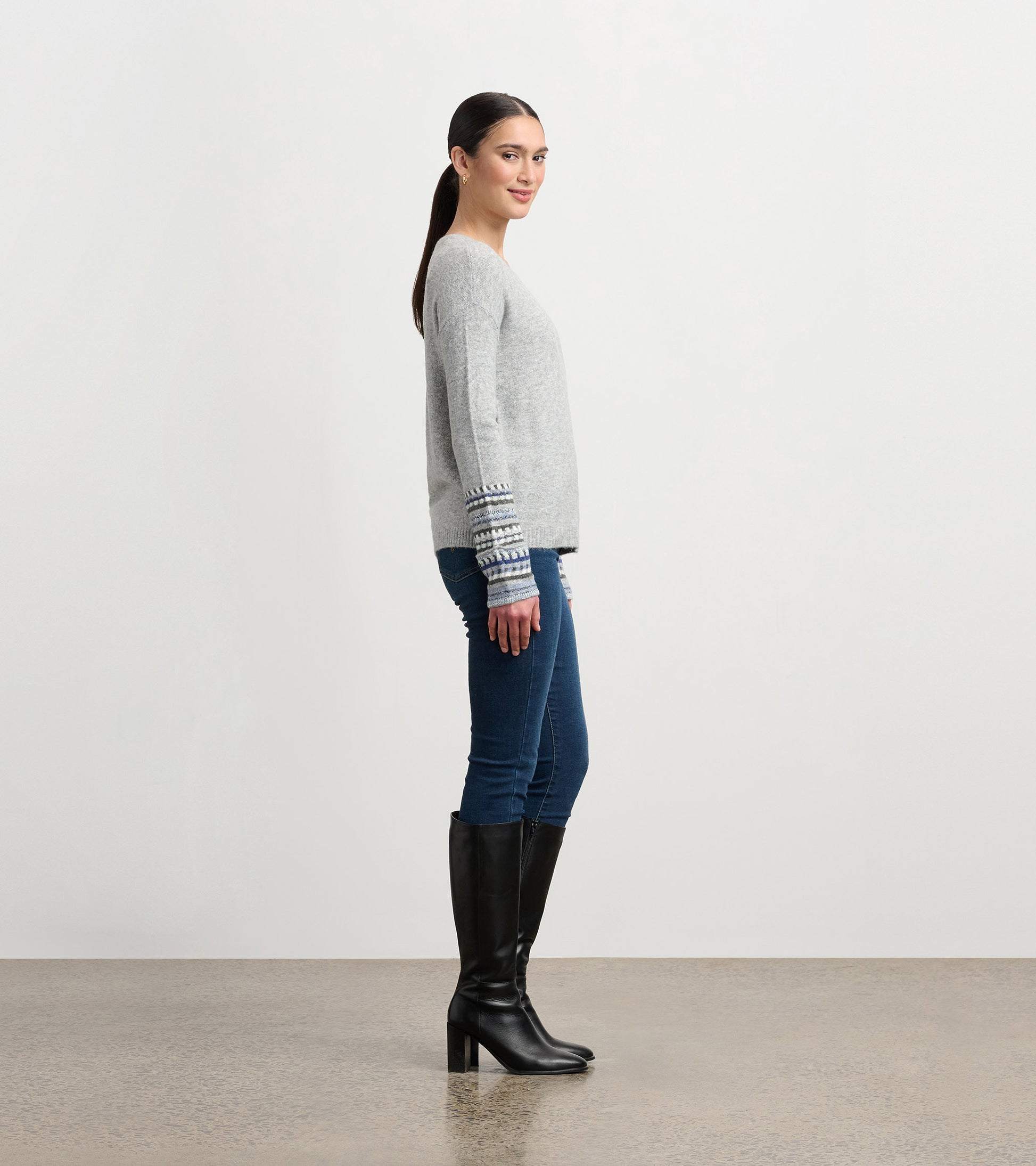 Grey melange sweater with patterned cuffs, featuring a relaxed fit, styled with blue jeans and knee-high black boots.