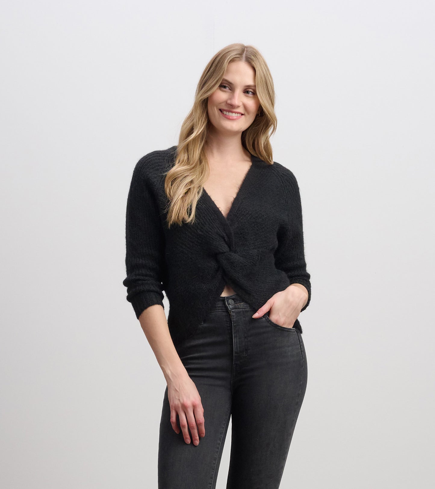 Black cross-over sweater with a textured finish and three-quarter sleeves, styled with high-waisted jeans.