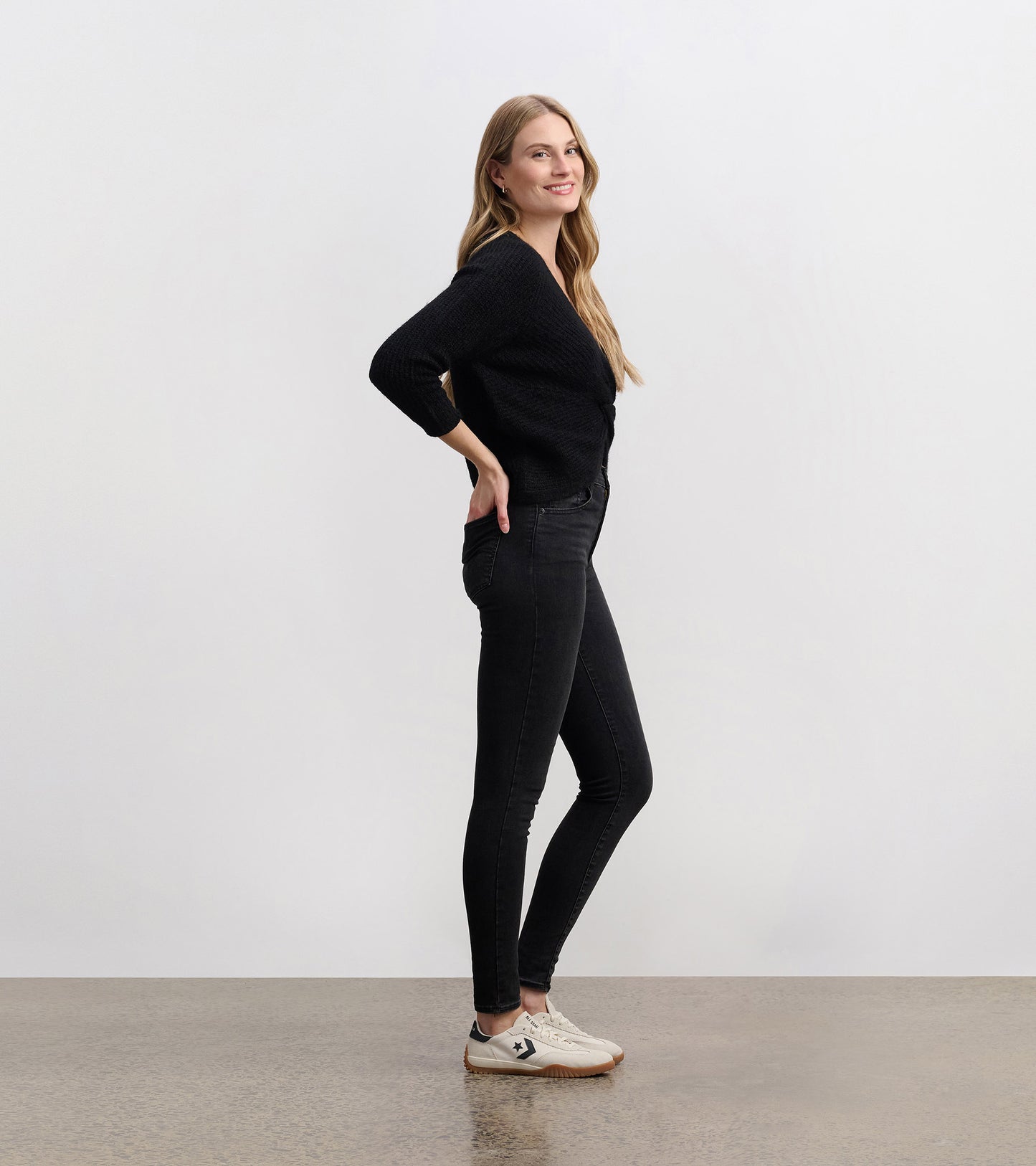 Black crossover sweater with a textured pattern, featuring three-quarter sleeves, styled with black jeans and sneakers.