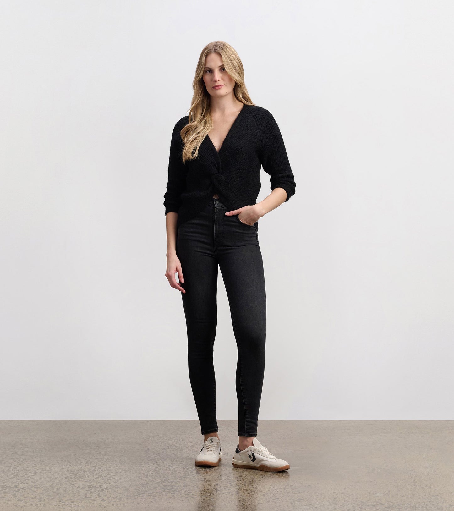 Black crossover sweater with a textured knit, featuring a deep V-neck and three-quarter sleeves, styled with skinny jeans.