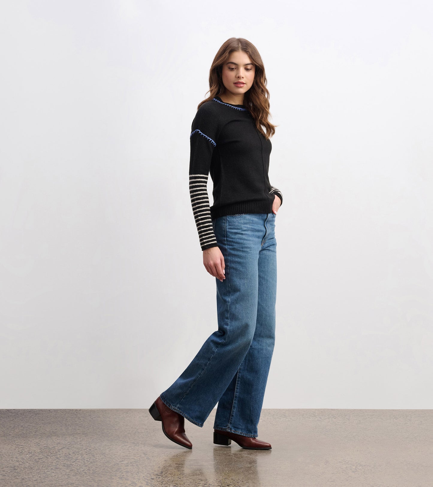 Black sweater with striped sleeves and blue stitching, paired with blue jeans and brown heeled boots.